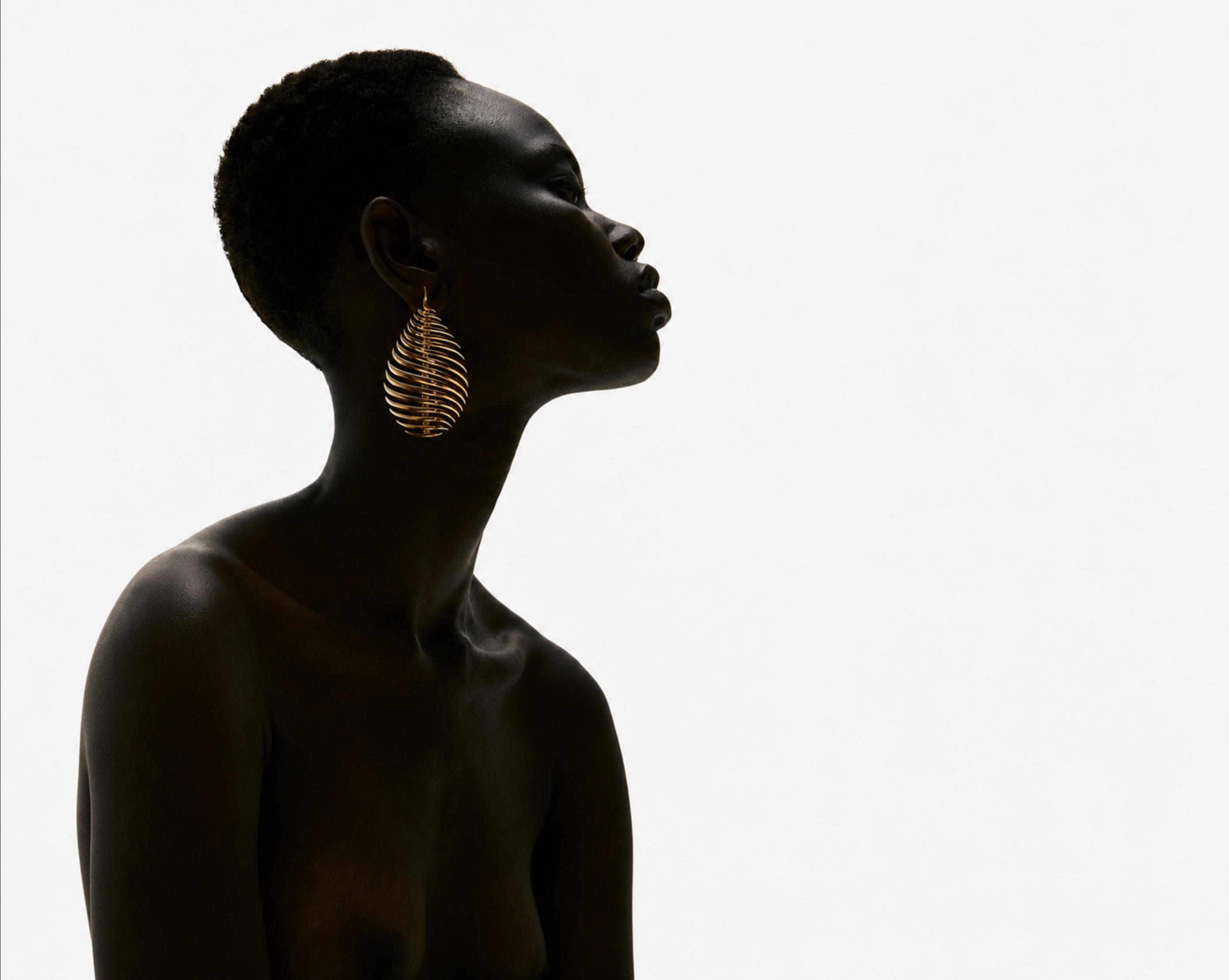 Side profile of a woman wearing a sculptural gold leaf earring against pale light