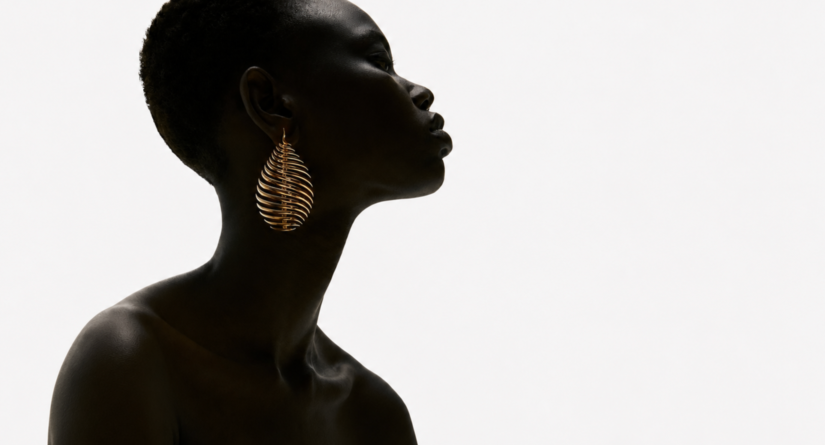 Side profile of a woman wearing a sculptural gold leaf earring against pale light