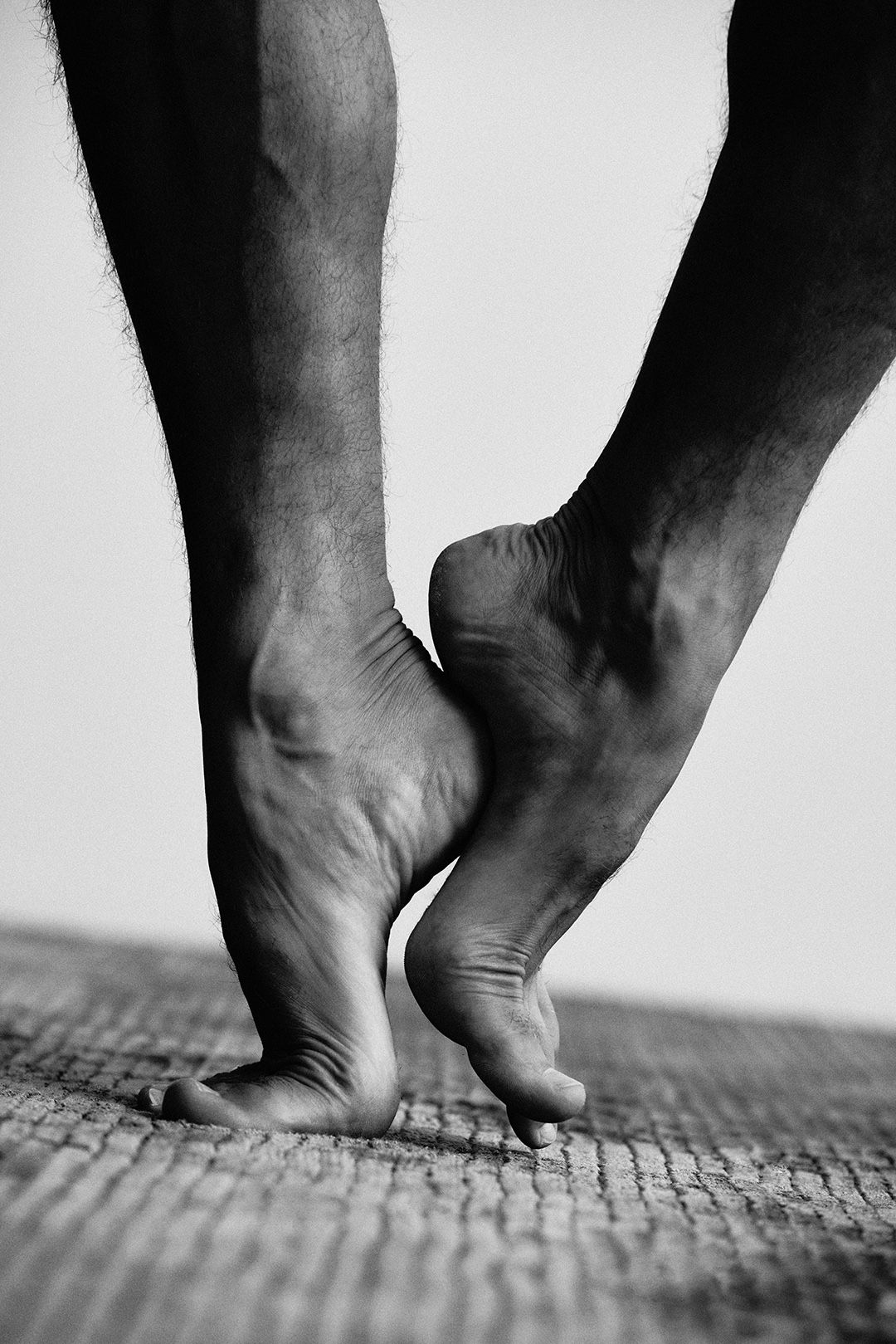 Close black-and-white study of a dancer's bare feet rising en pointe on cobblestones