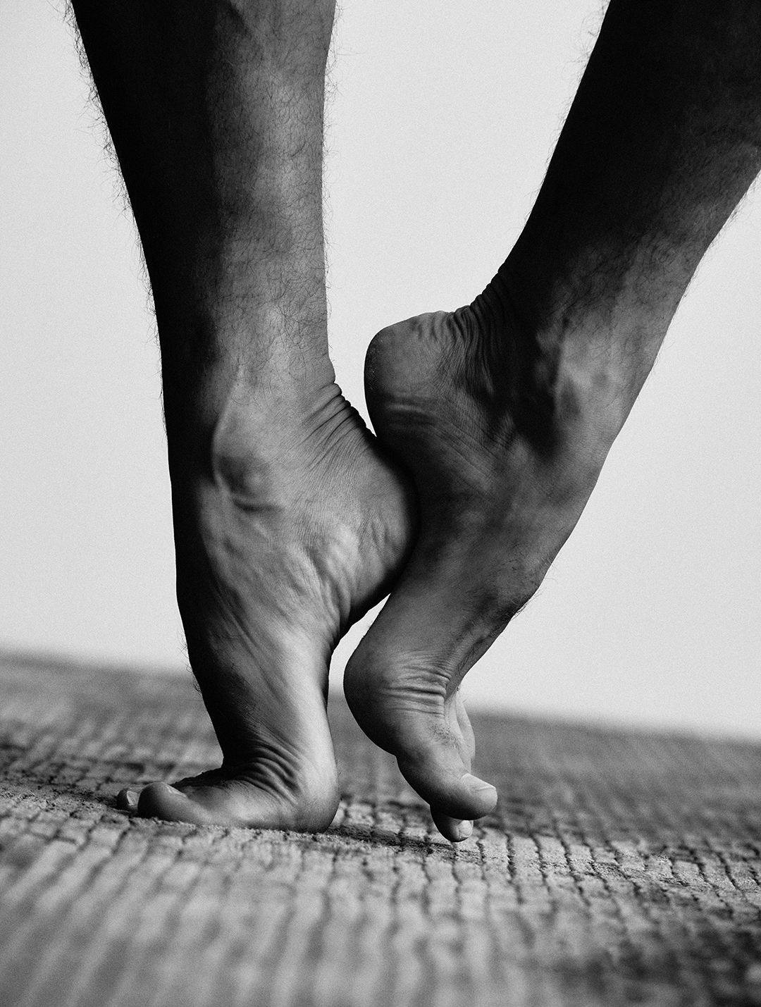 Close black-and-white study of a dancer's bare feet rising en pointe on cobblestones