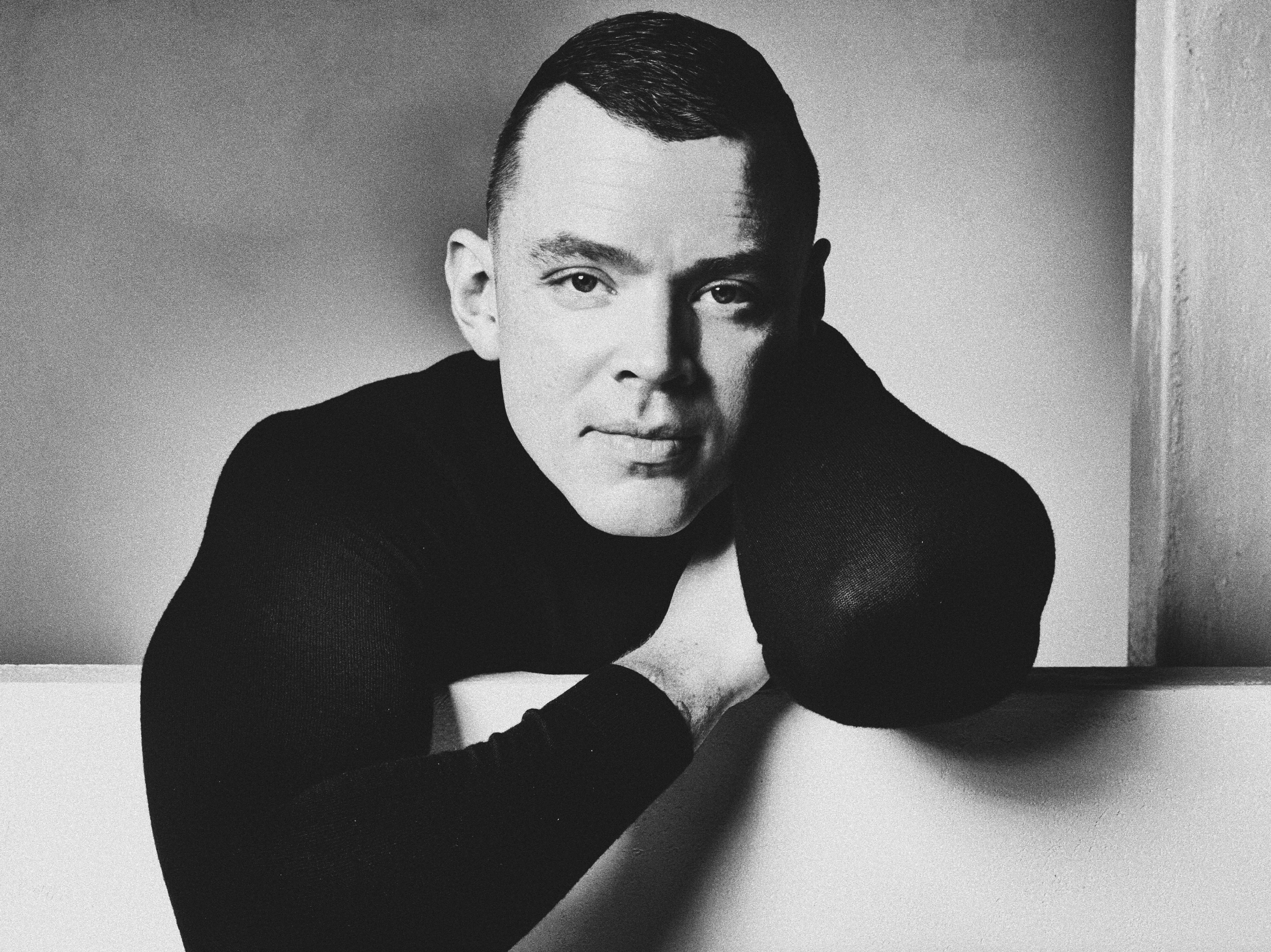 Black-and-white studio portrait of a man in a dark roll-neck, chin resting on hand