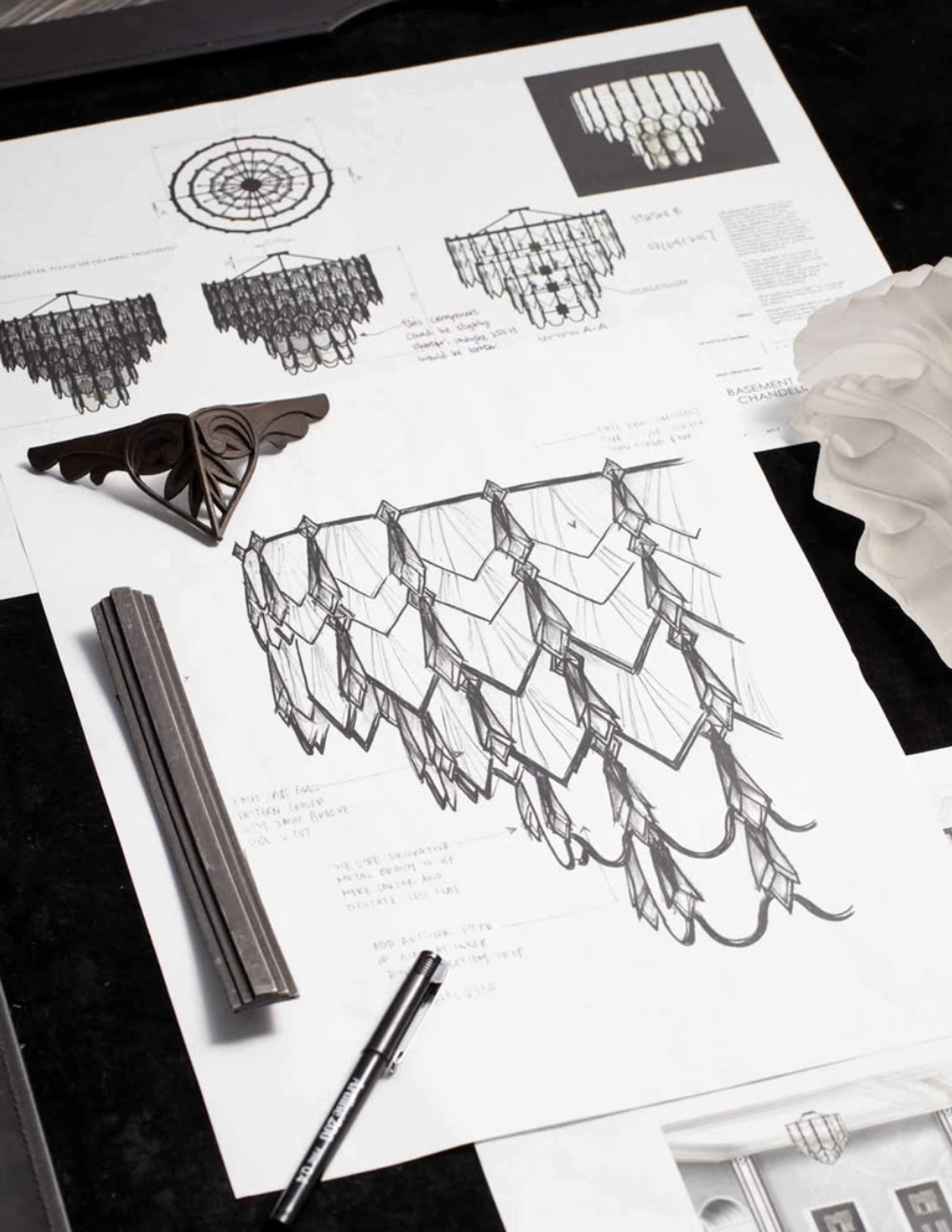 Detailed hand-drawn design sketches for a crystal chandelier laid out with a pencil and bust