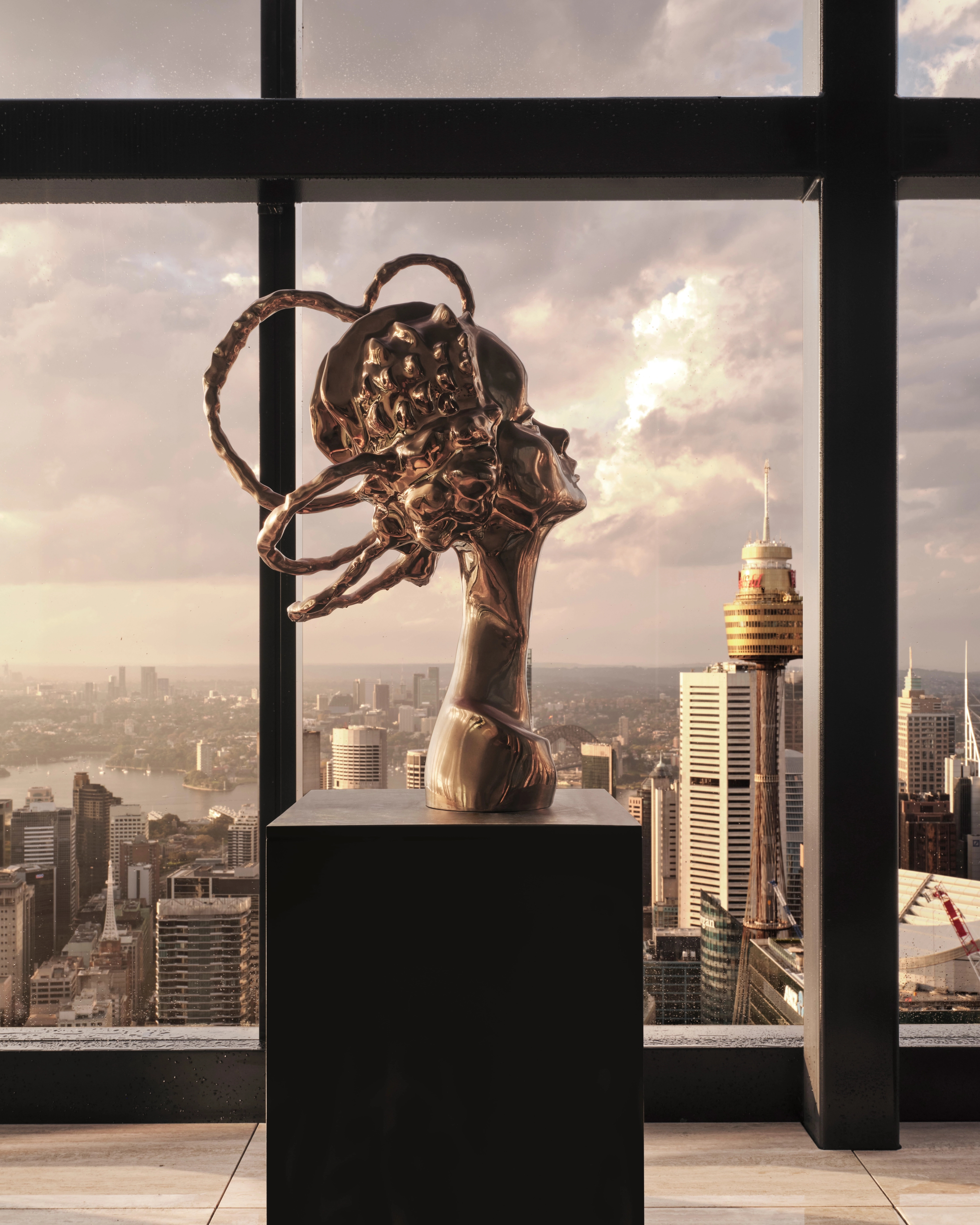 Bronze abstract head on a plinth silhouetted against a dusk city skyline