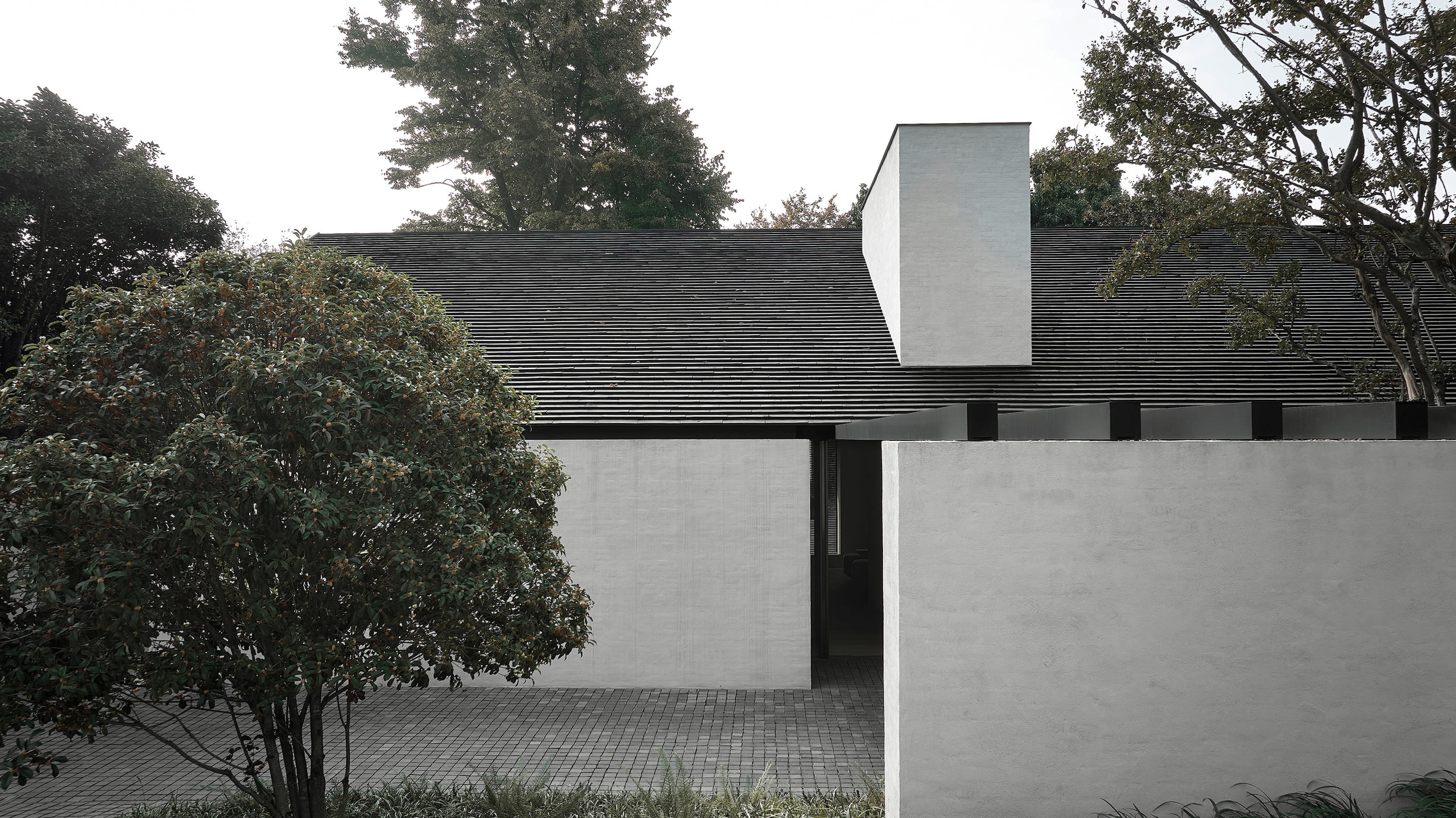 Dark-shingled pavilion with a sculptural white chimney form among trees, by Vincent Van Duysen