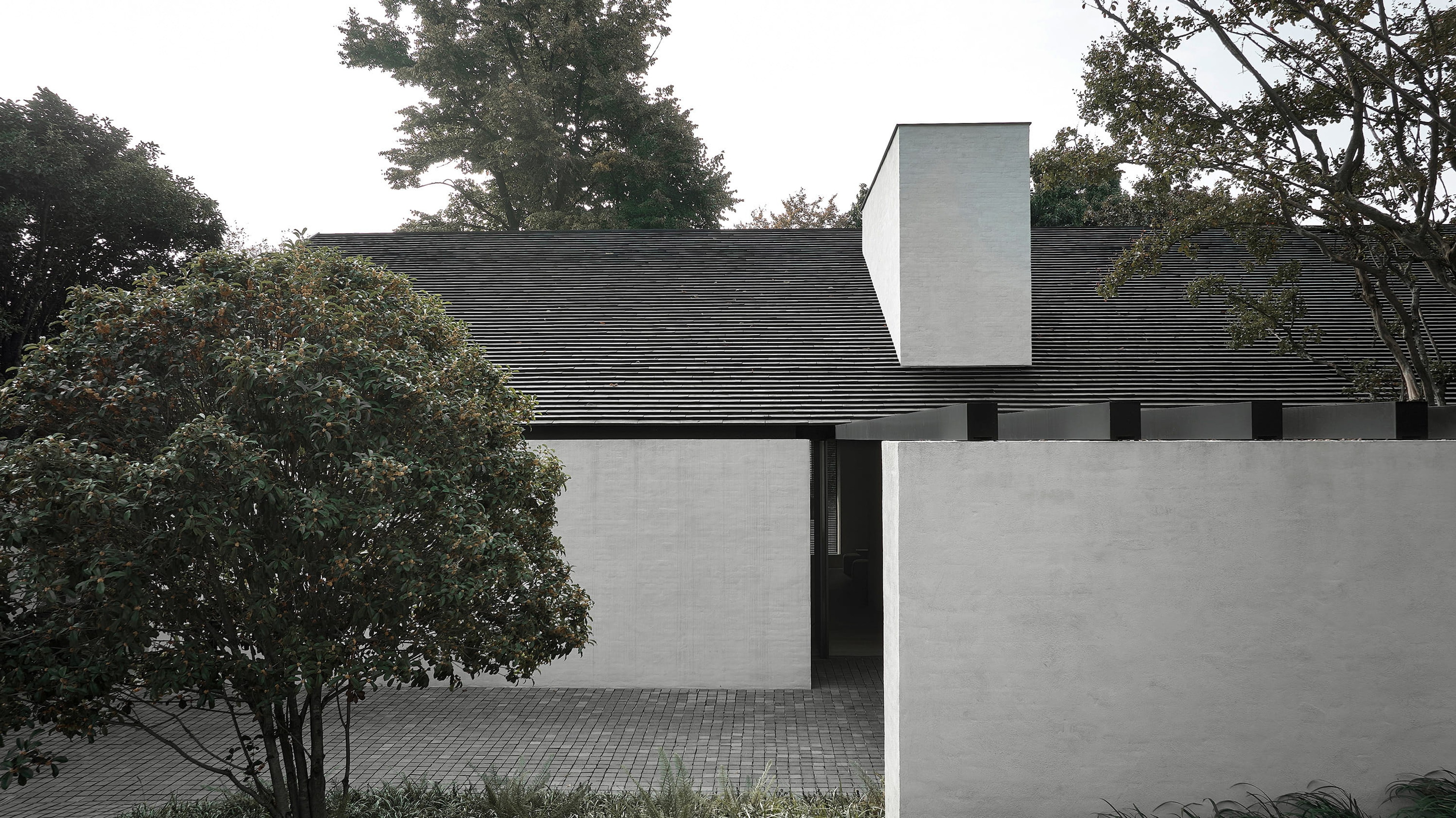 Dark-shingled pavilion with a sculptural white chimney form among trees, by Vincent Van Duysen