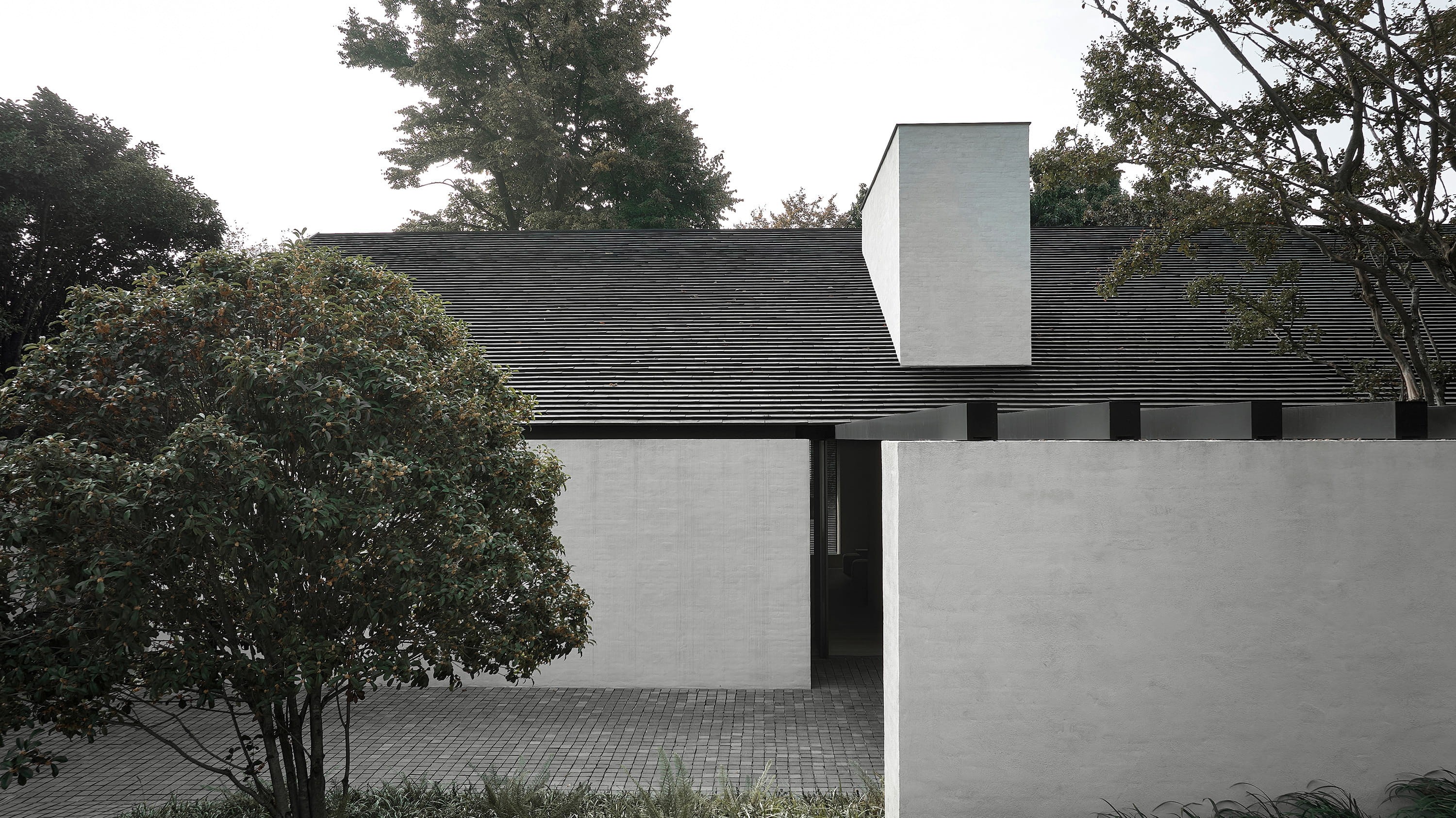 Dark-shingled pavilion with a sculptural white chimney form among trees, by Vincent Van Duysen
