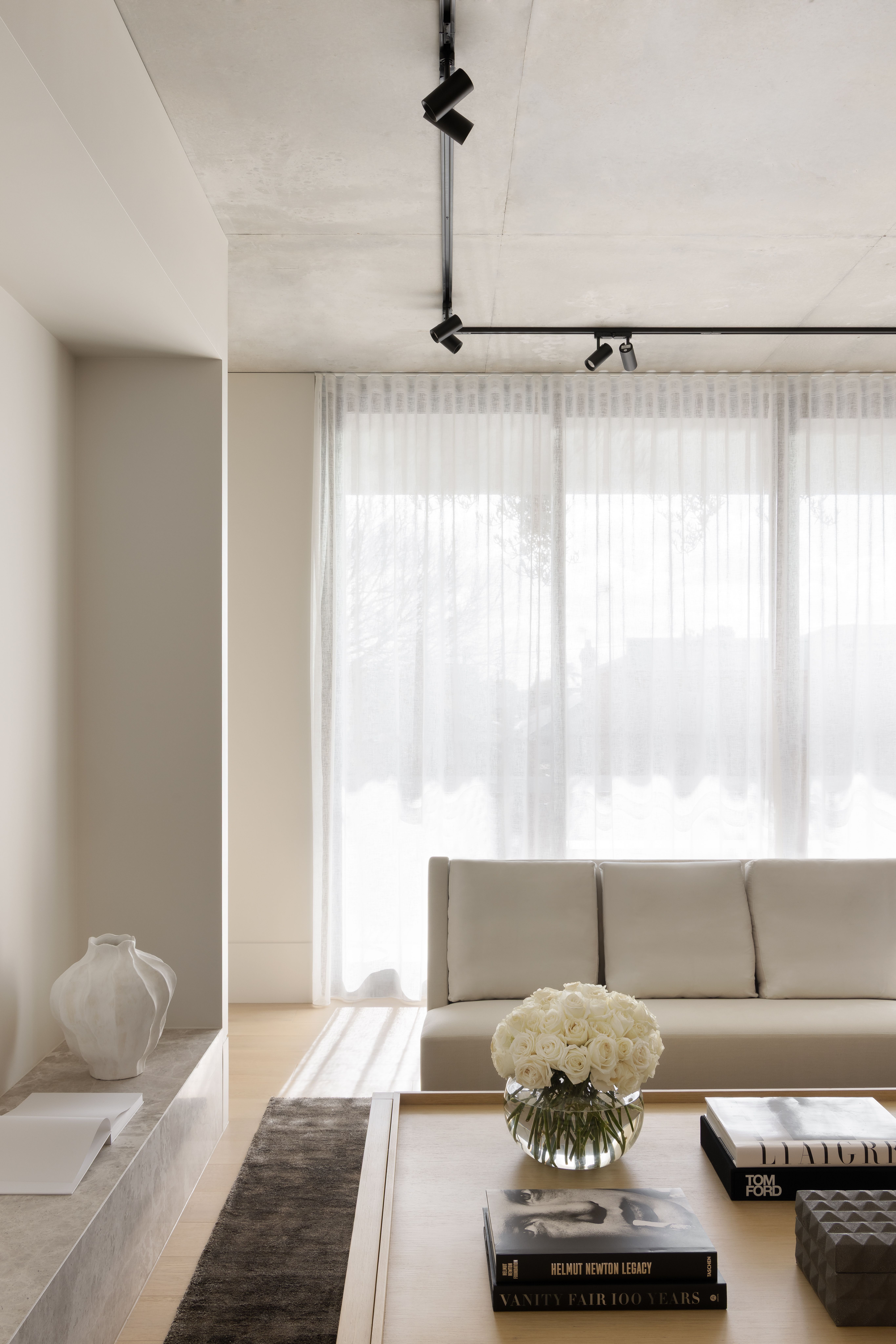 Bright living room with a low sofa, sheer curtains and books stacked beside white blooms