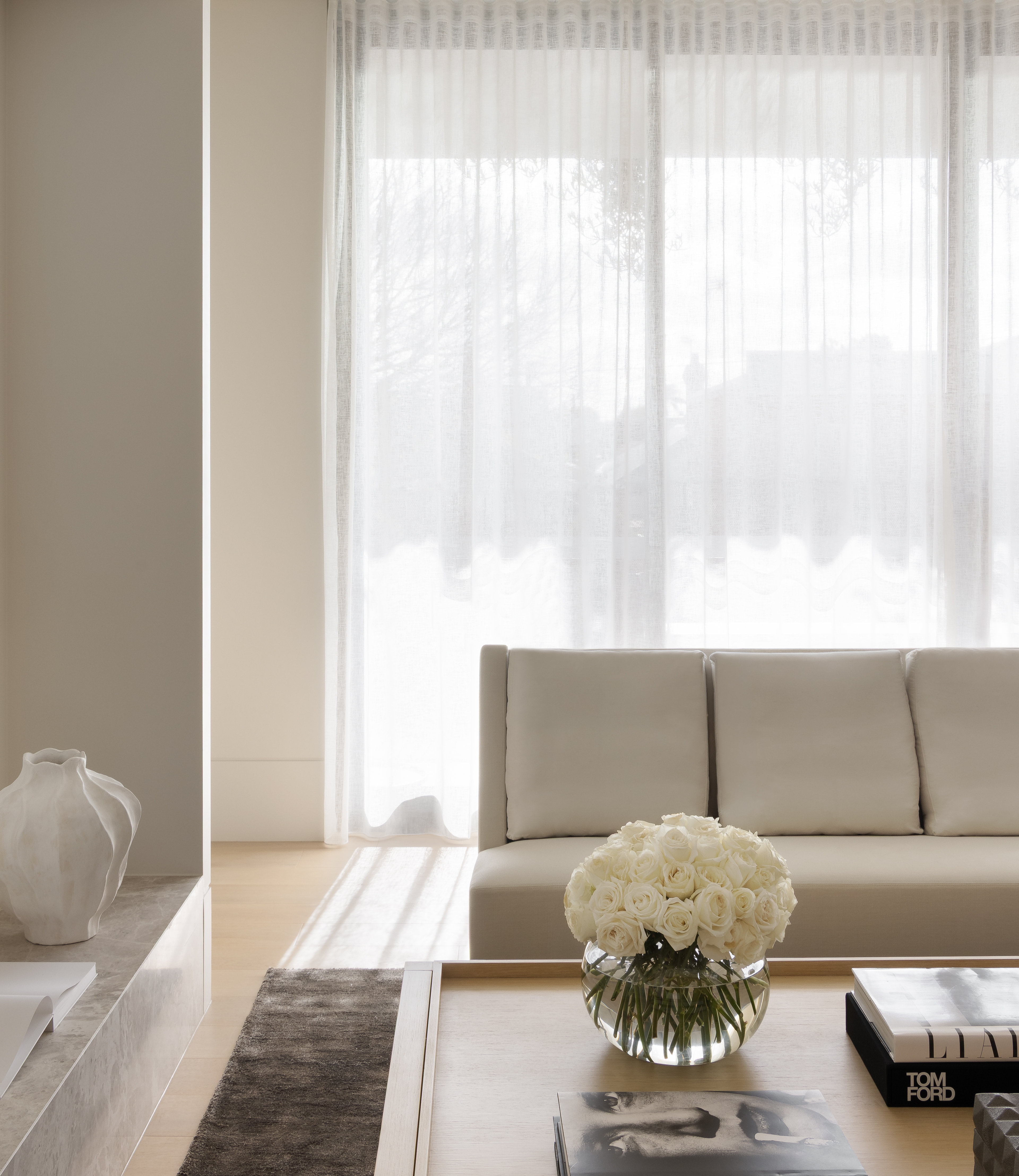 Bright living room with a low sofa, sheer curtains and books stacked beside white blooms