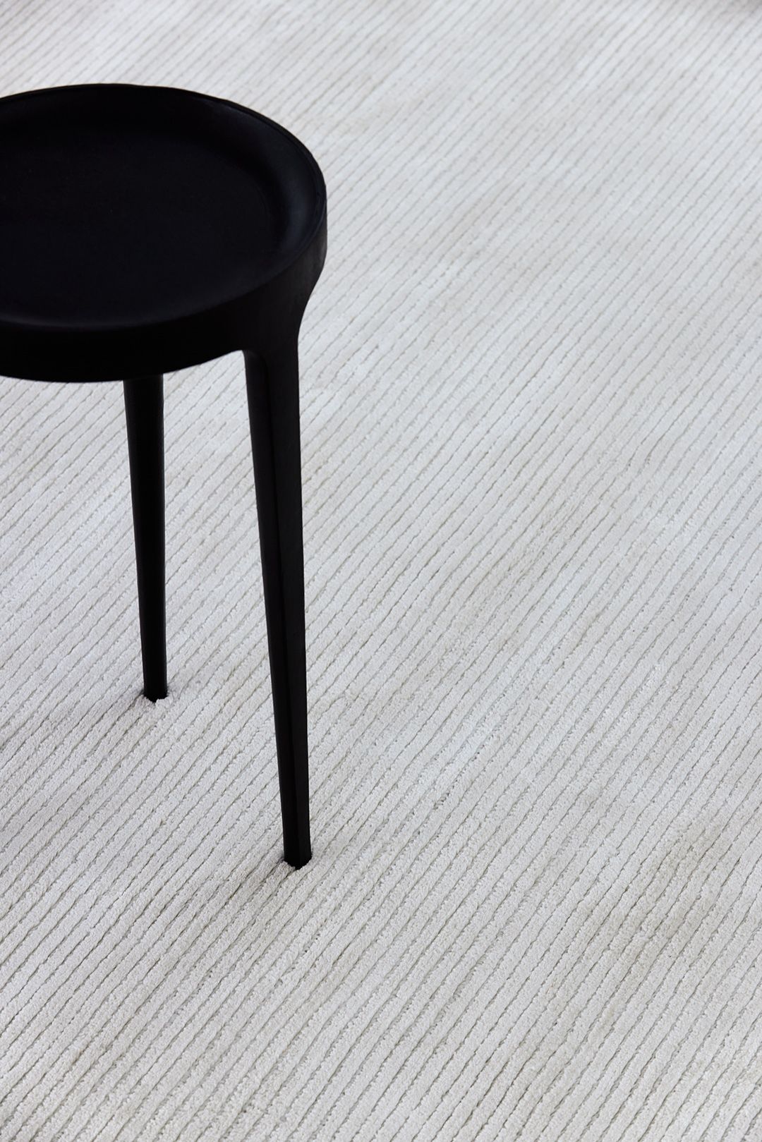 Sculptural black pedestal stool resting on a finely ribbed pale rug