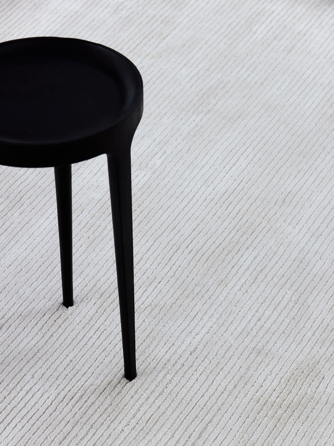Sculptural black pedestal stool resting on a finely ribbed pale rug