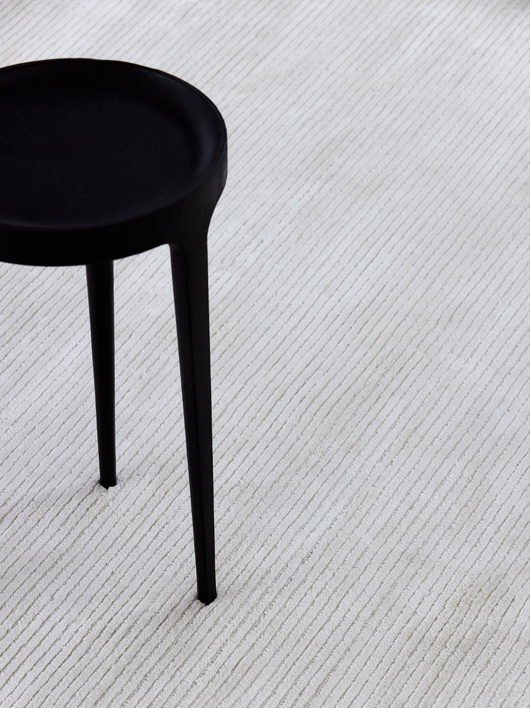 Sculptural black pedestal stool resting on a finely ribbed pale rug