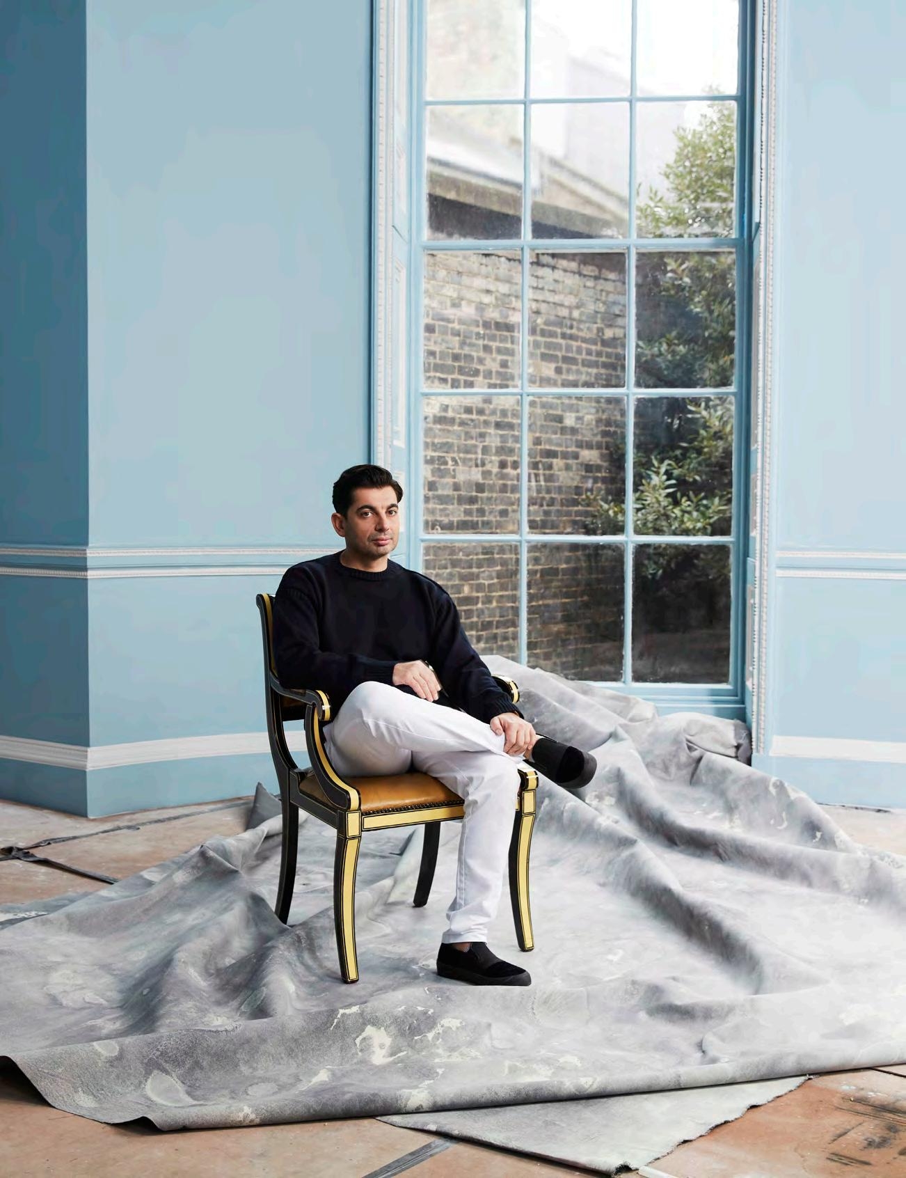 Man seated on a gilt chair over a draped hide beside a tall arched window