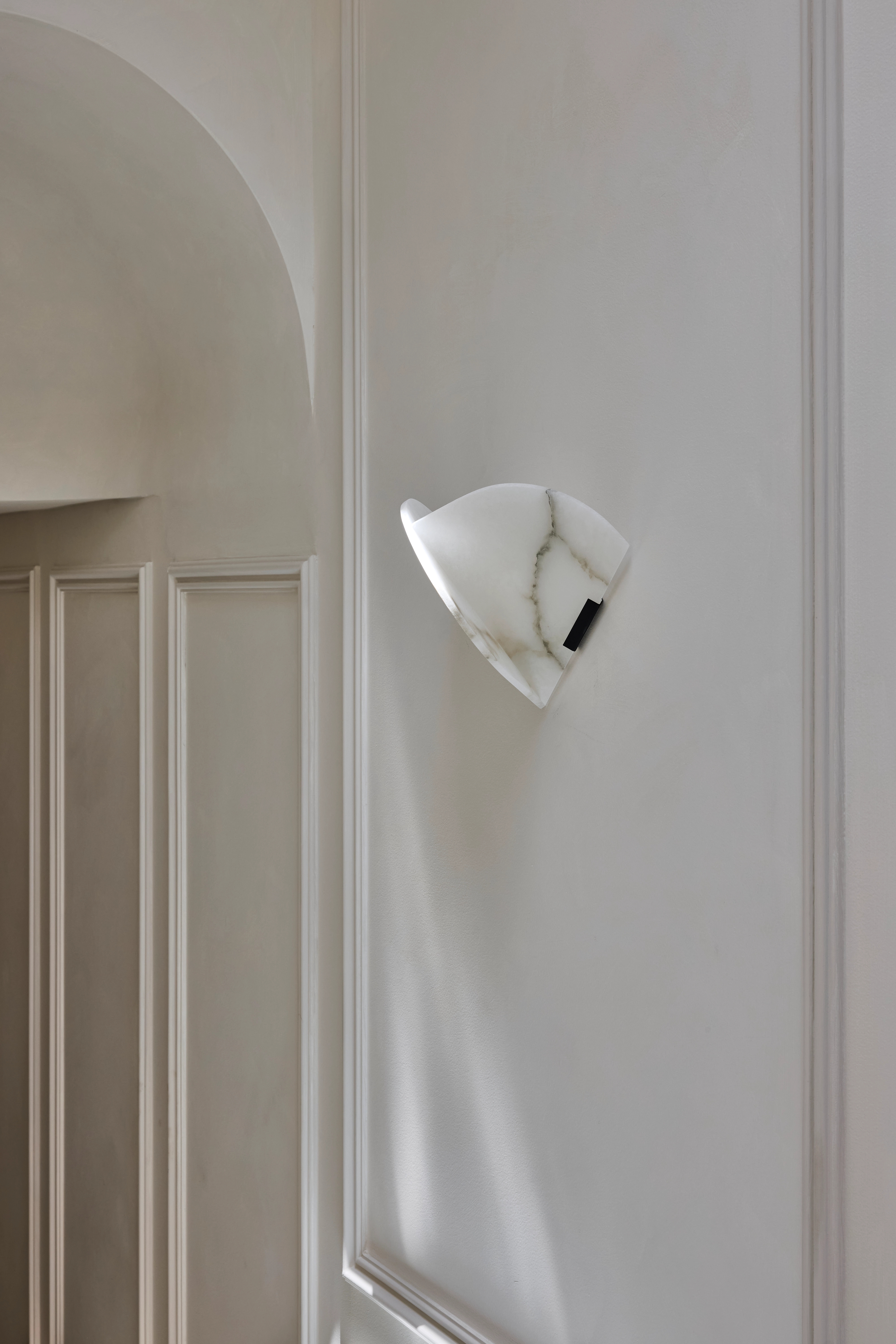 Sculptural white wall light casting soft shadow across a panelled niche