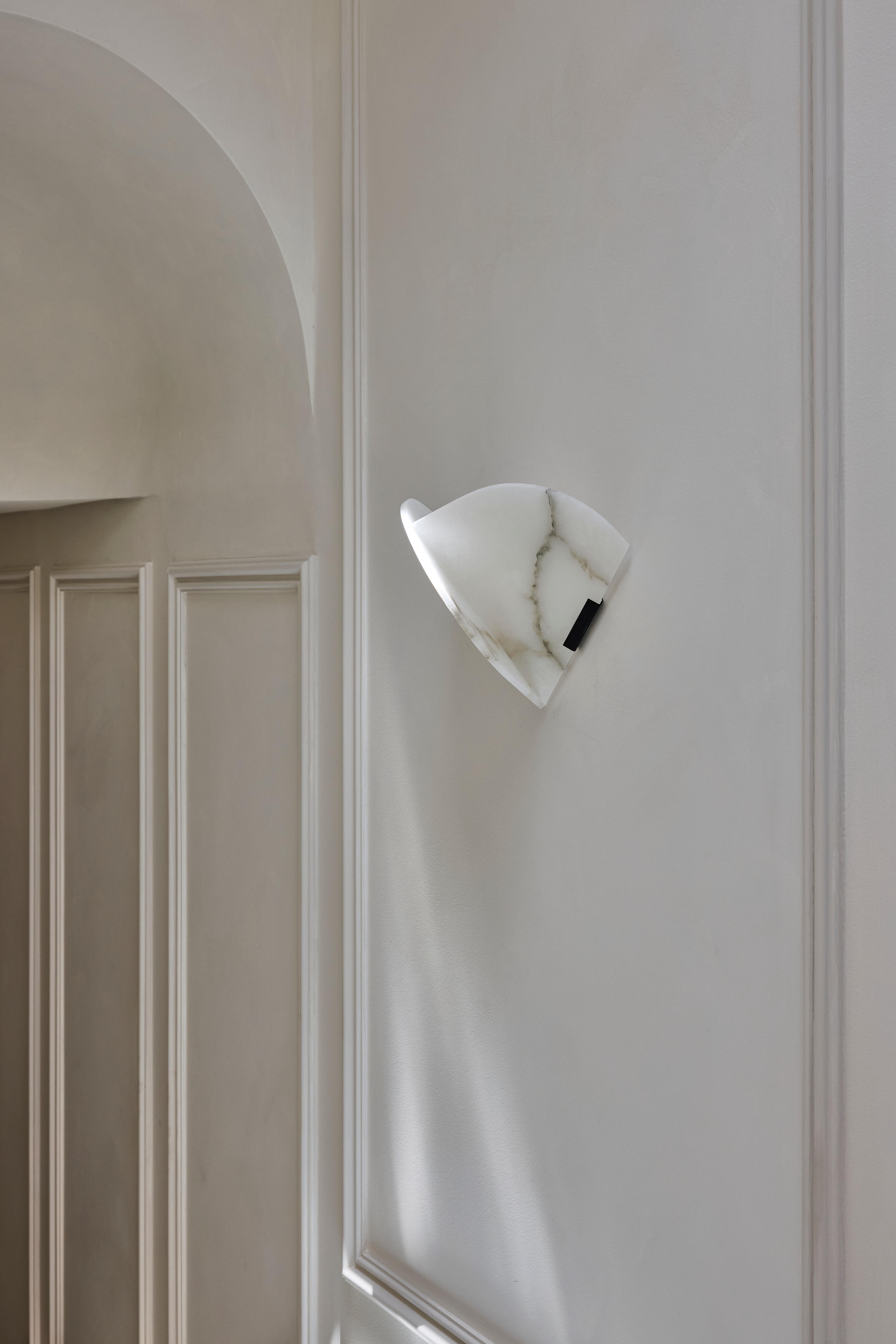 Sculptural white wall light casting soft shadow across a panelled niche