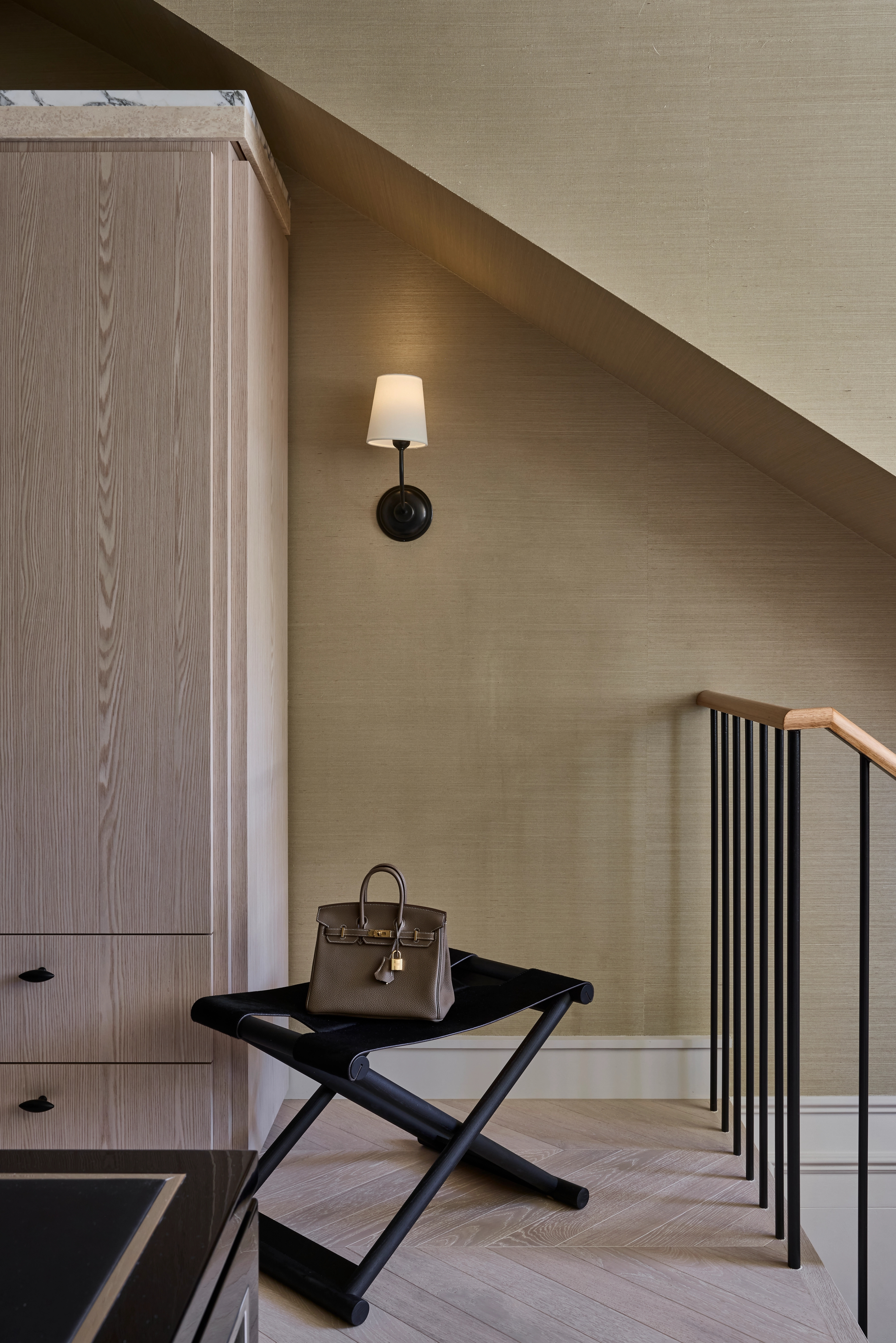 Softly lit stair landing with a folding stool and a tan leather handbag