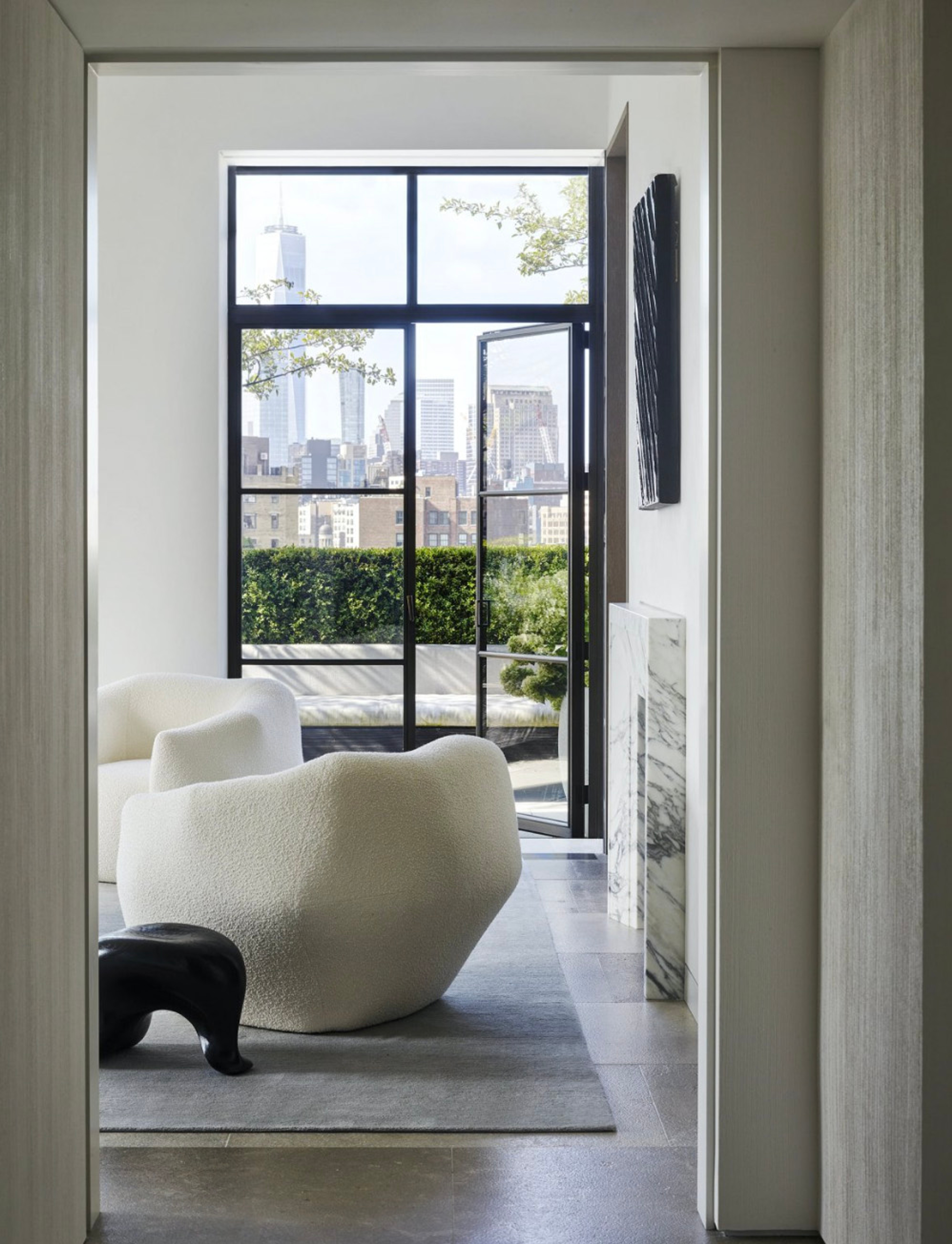 Bouclé armchair beside a marble side table framed by a black-steel window and city view