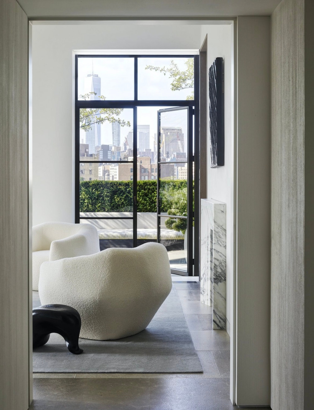 Bouclé armchair beside a marble side table framed by a black-steel window and city view