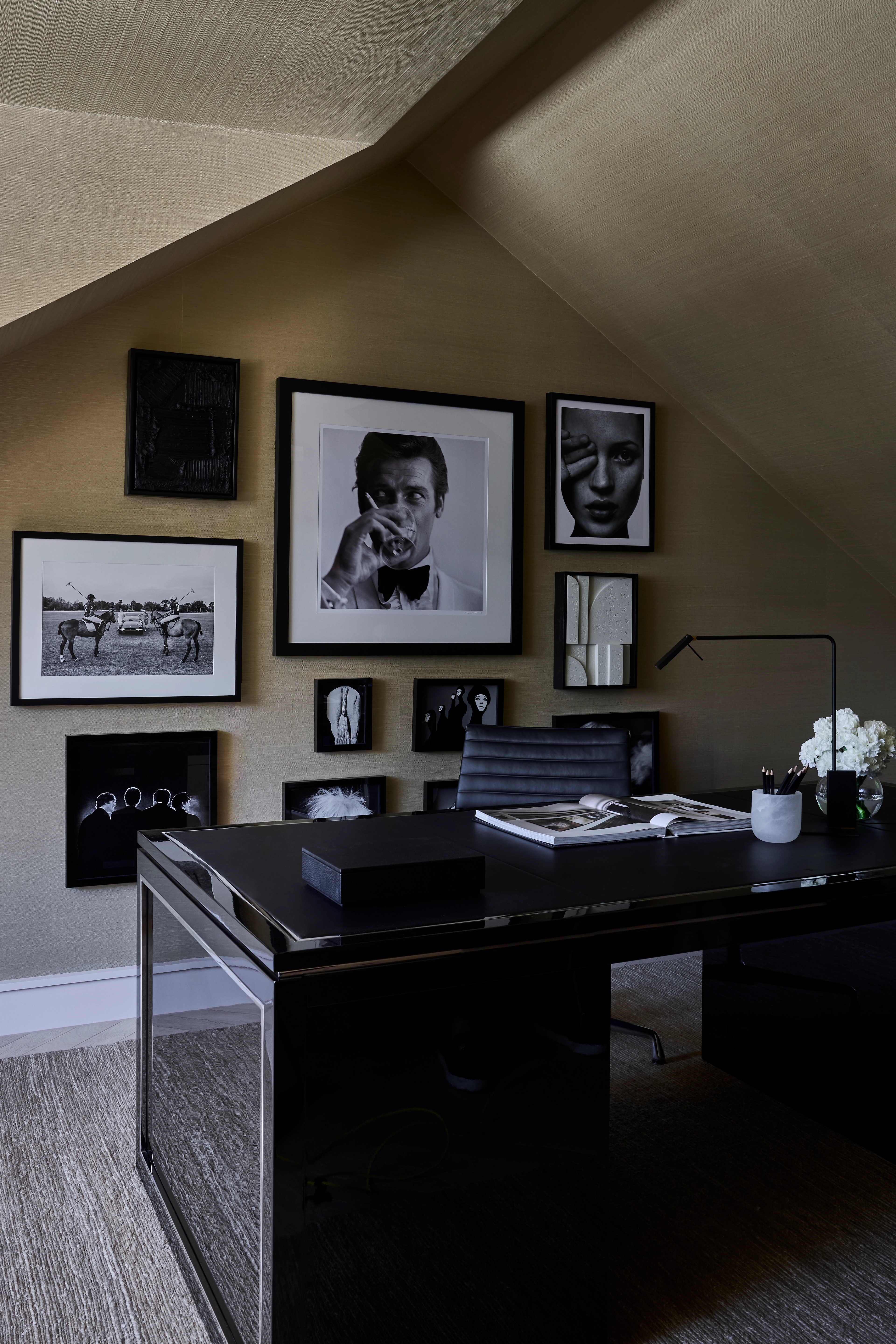 Attic study beneath a sloped ceiling with a black desk and a gallery wall of photographs