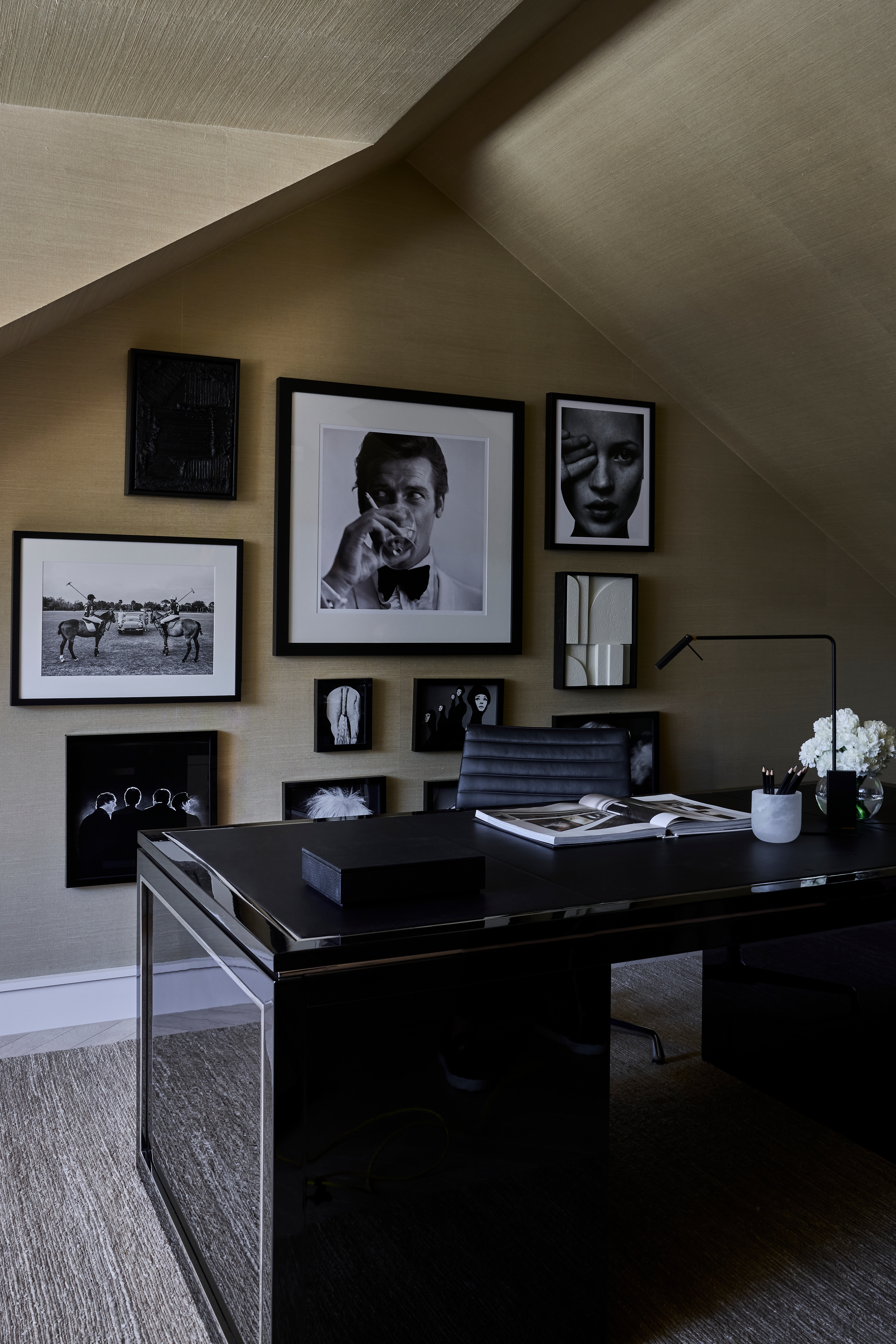 Attic study beneath a sloped ceiling with a black desk and a gallery wall of photographs