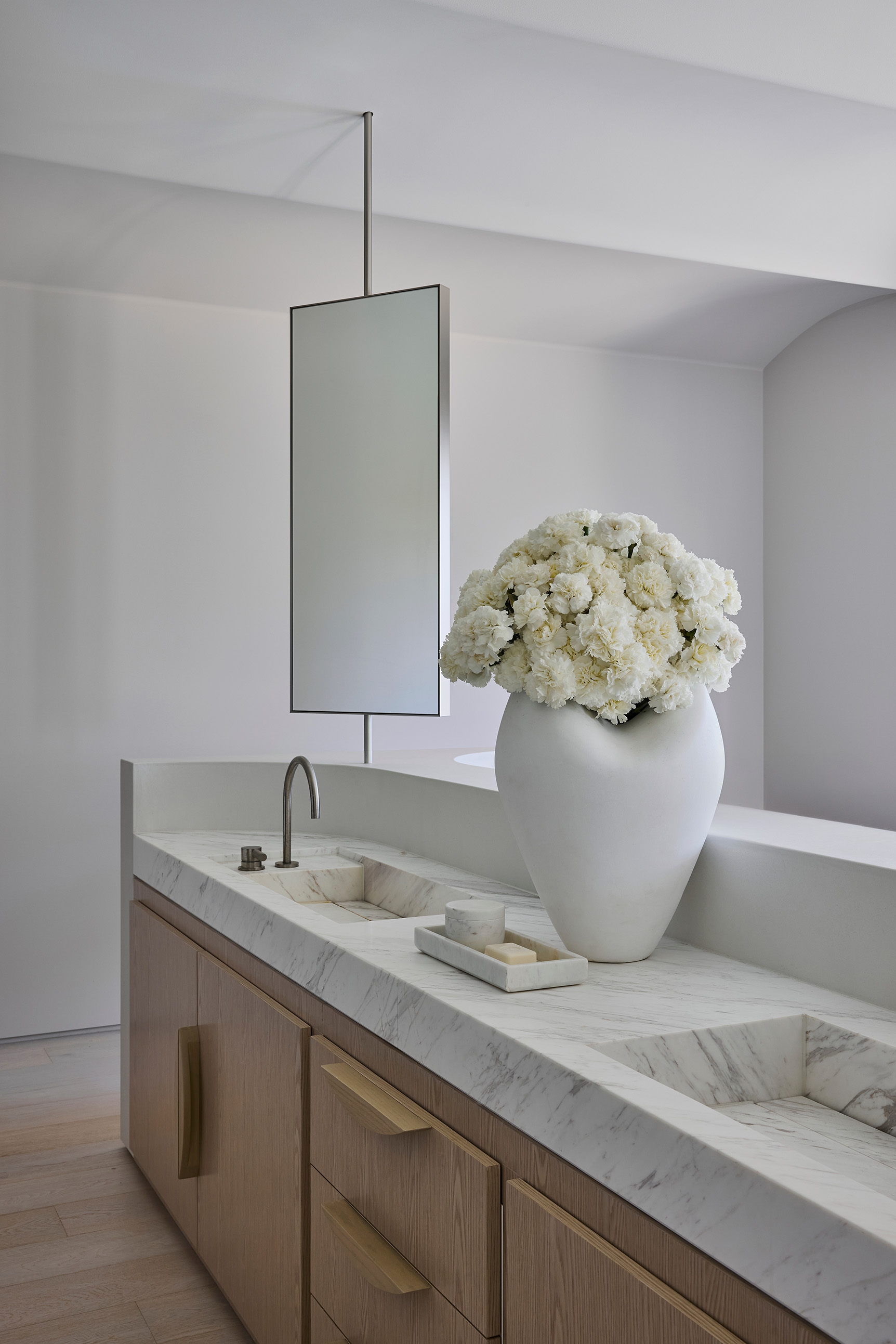 Marble-topped timber vanity with a tall frameless mirror and white hydrangeas