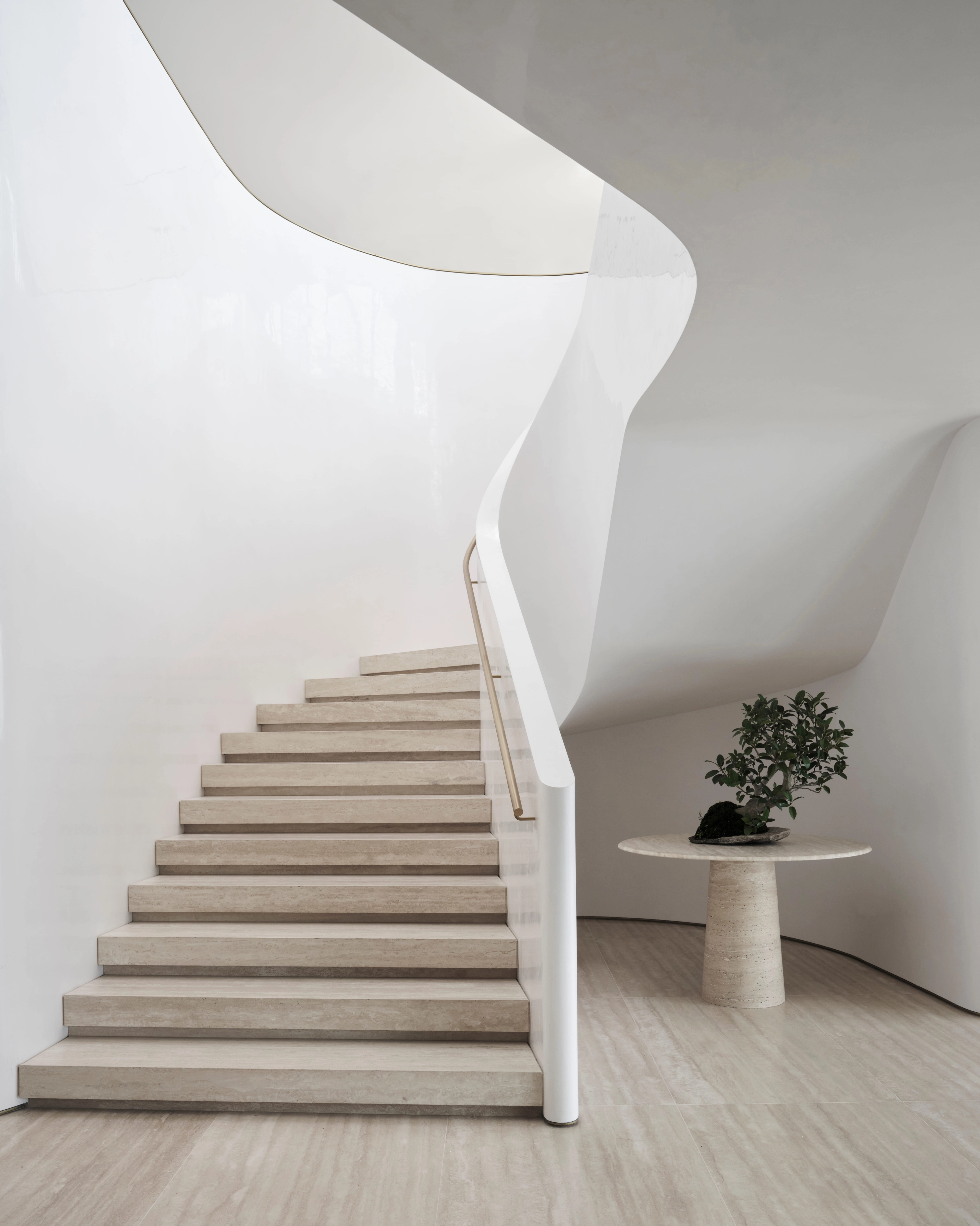 Curving pale staircase by Freeman & Co rising above travertine beside a round pedestal table