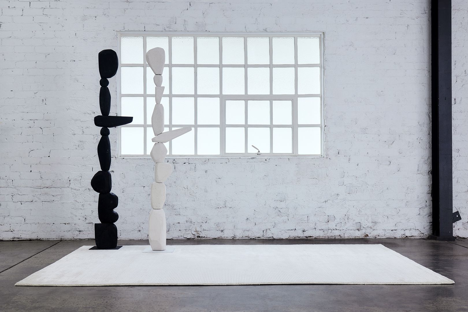 Two stacked totem sculptures, one black and one pale, before a gridded studio window