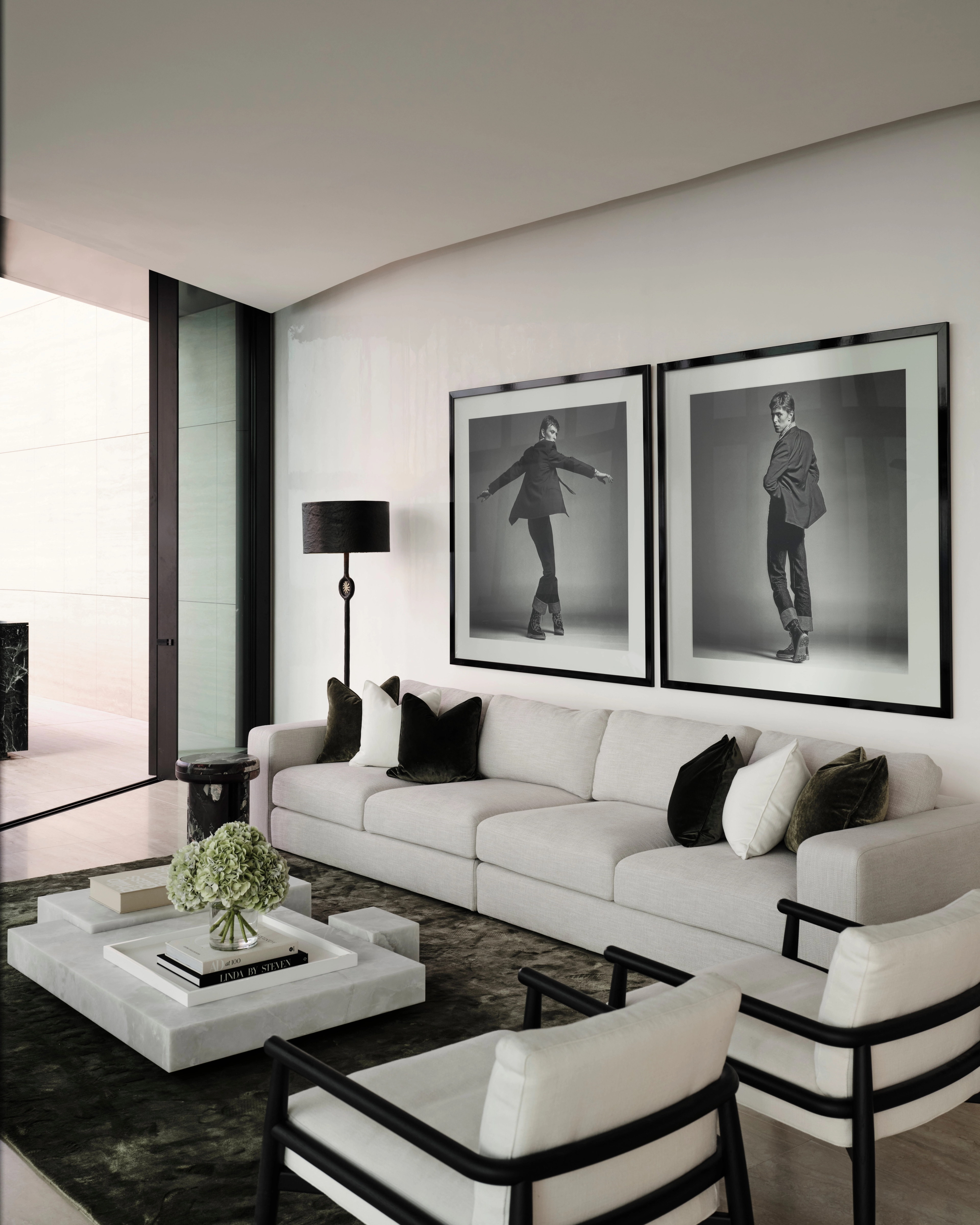Monochrome living room with paired fashion photographs and low white seating, by Freeman & Co