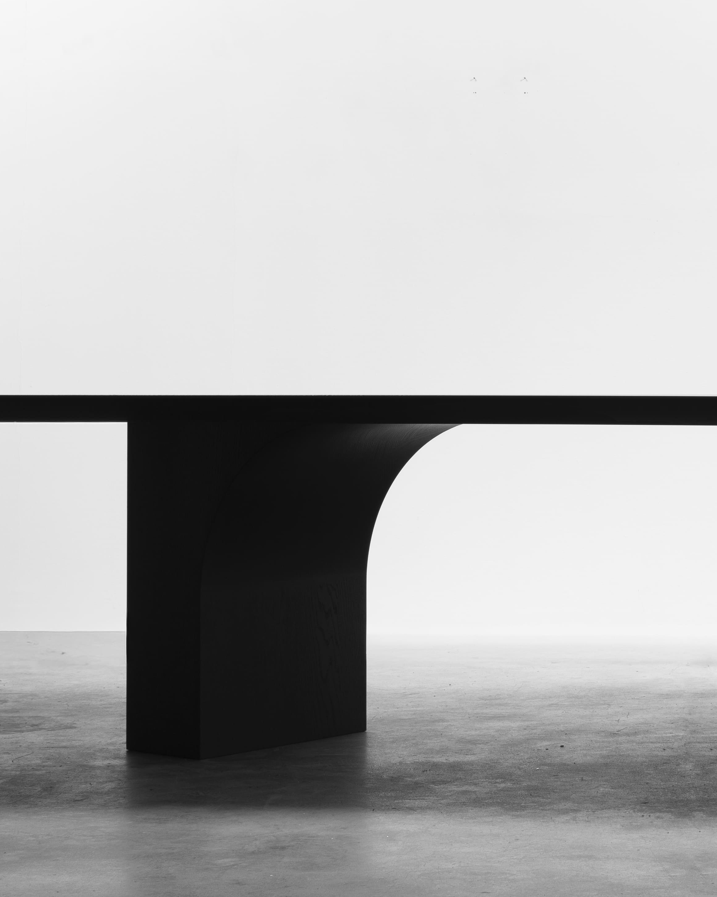Minimalist black arch-form bench by Freeman & Co floating against white on polished concrete