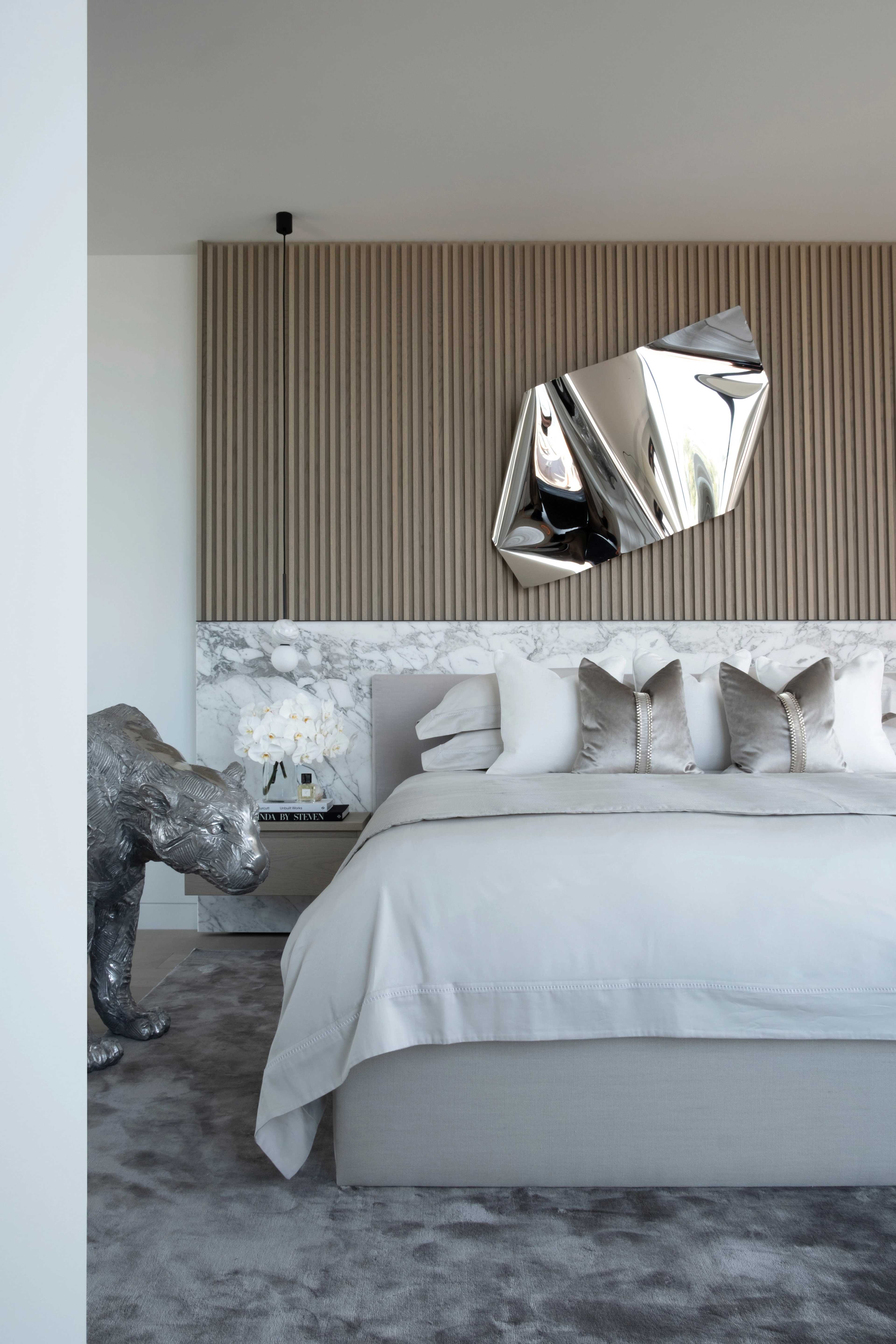 Tranquil bedroom by Freeman & Co with a mirror-polished wall sculpture and crouching bronze animal