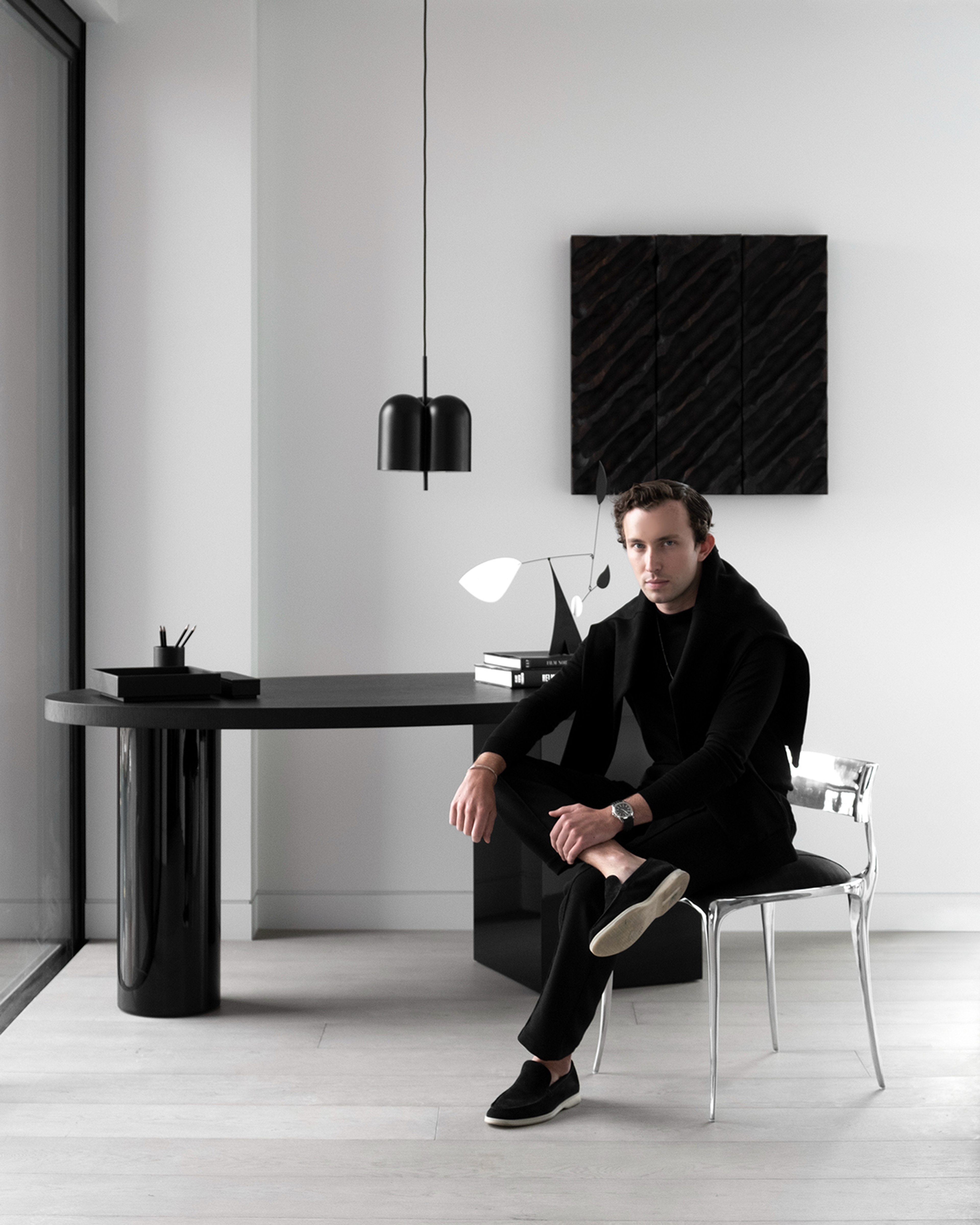 Man in black seated at a monolithic pedestal desk in a pared-back study