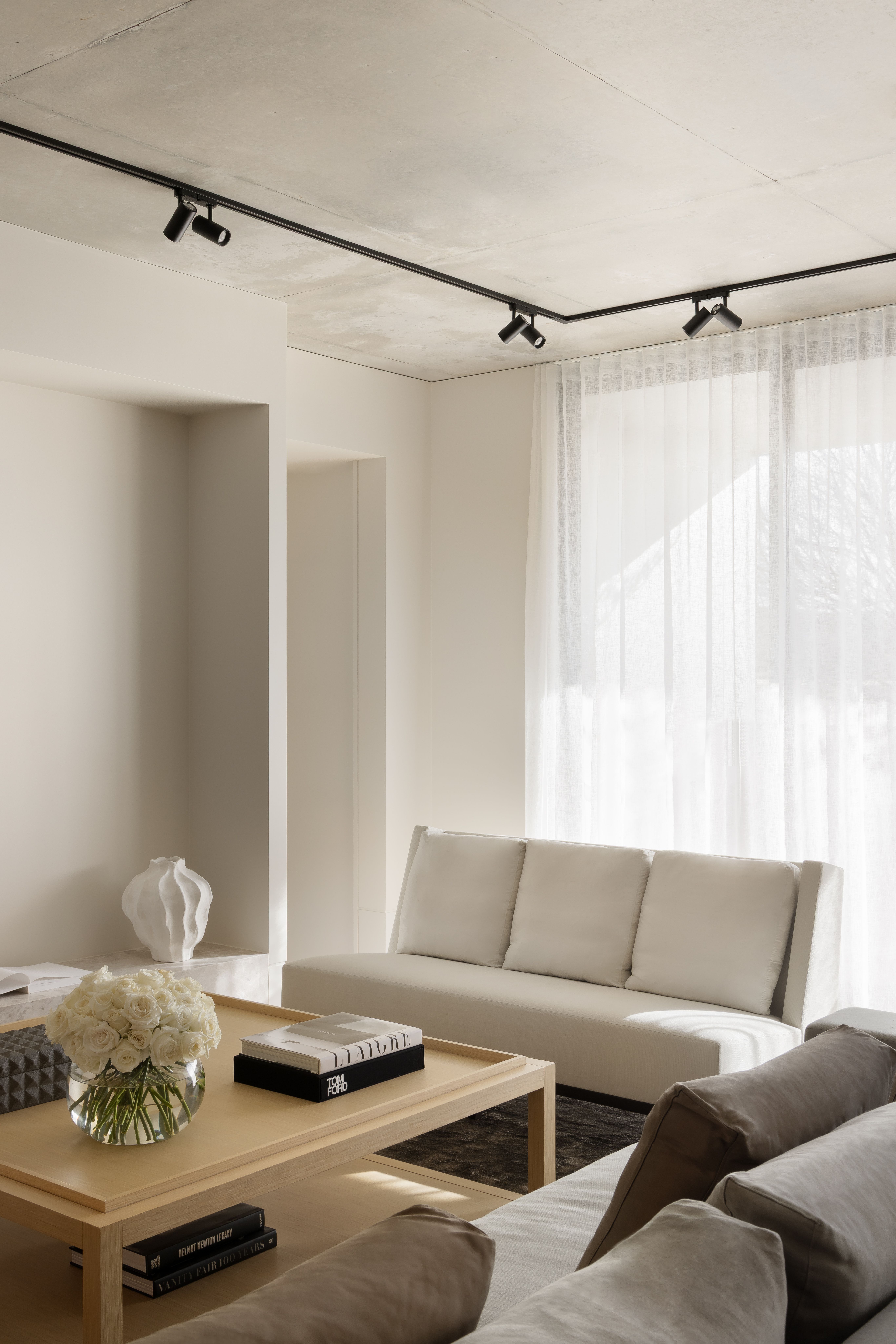 Softly lit sitting room with a cream sofa, low timber table and sheer-curtained windows