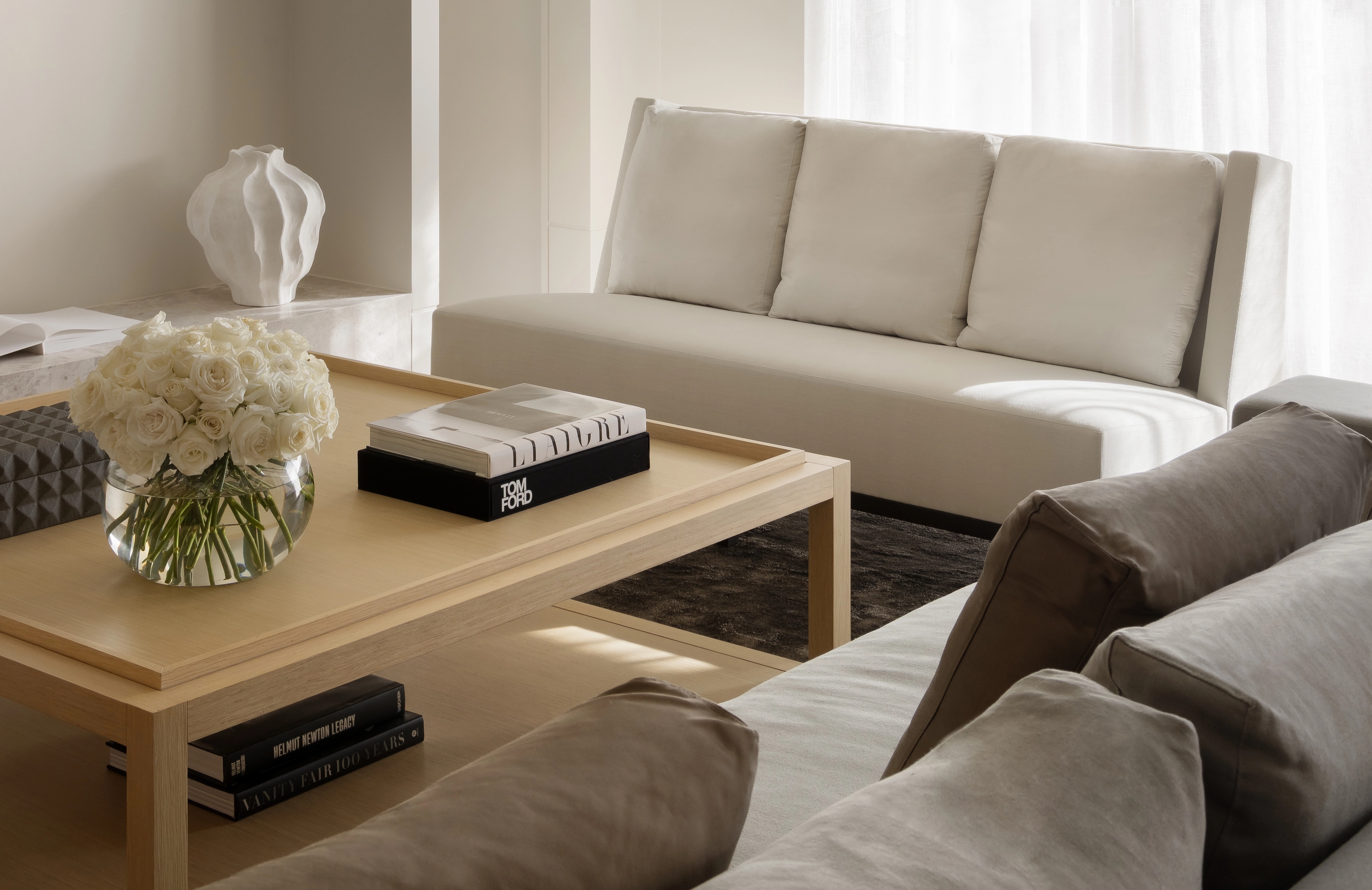 Softly lit sitting room with a cream sofa, low timber table and sheer-curtained windows