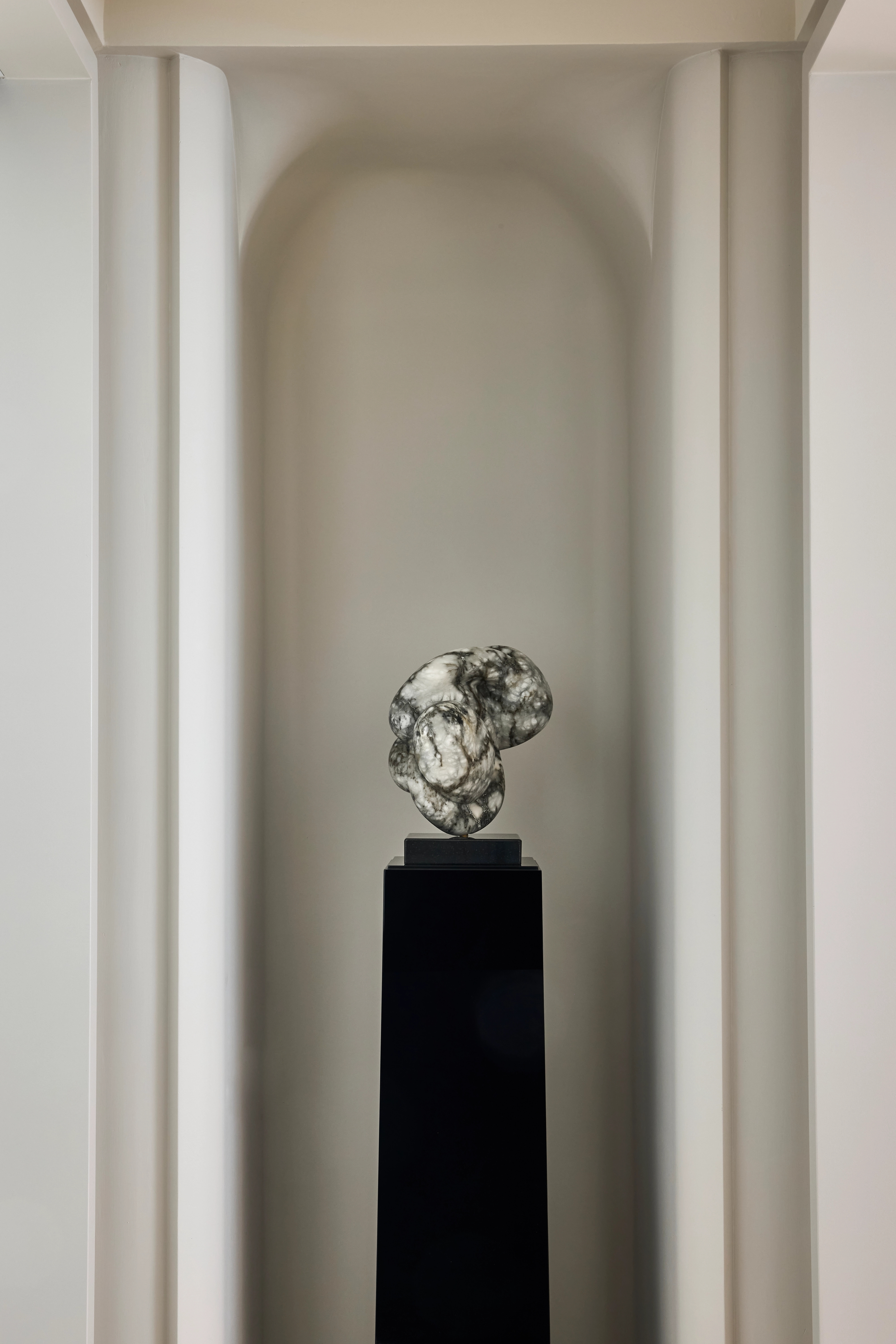 Polished chrome sculpture on a black plinth set within an arched wall niche
