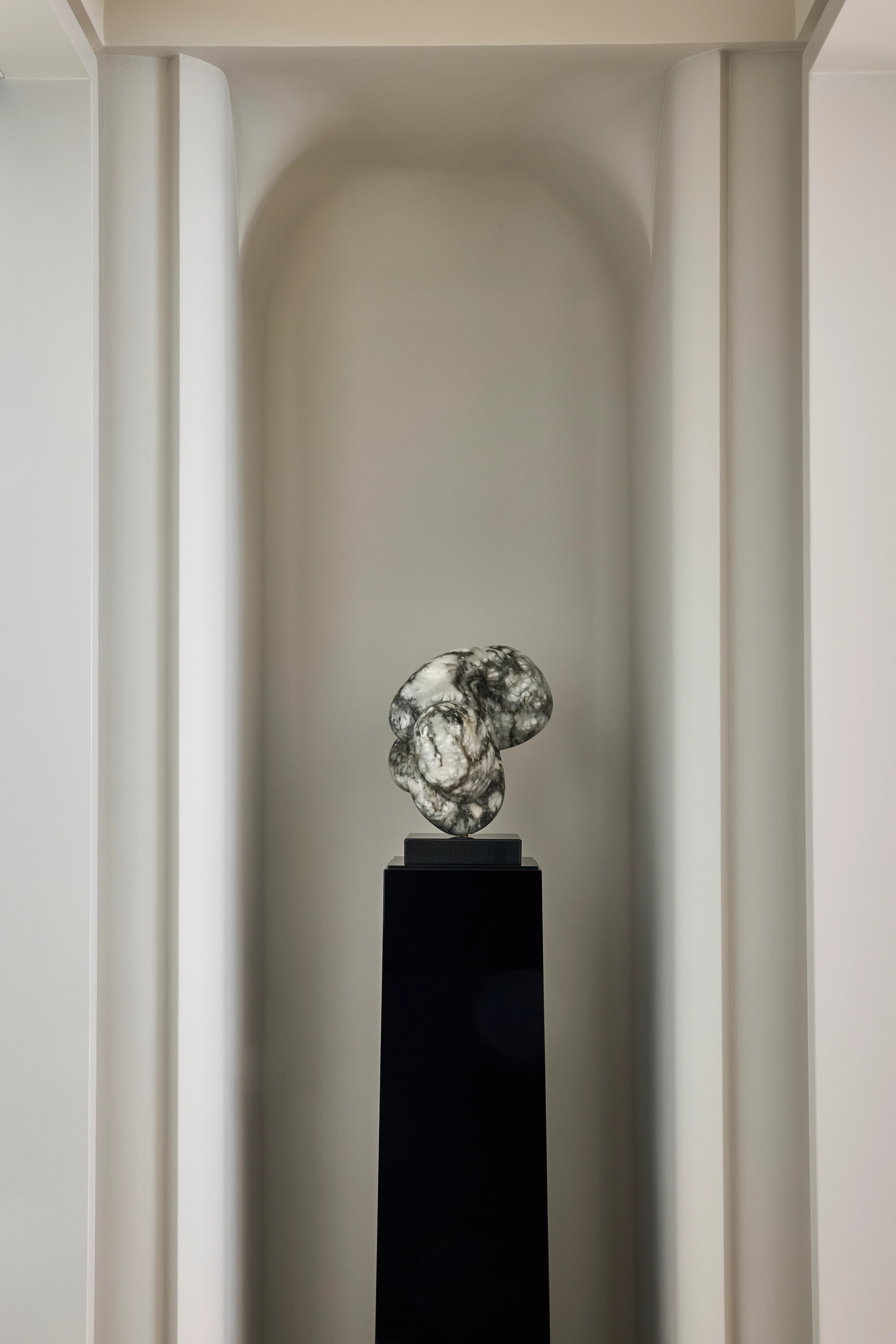 Polished chrome sculpture on a black plinth set within an arched wall niche