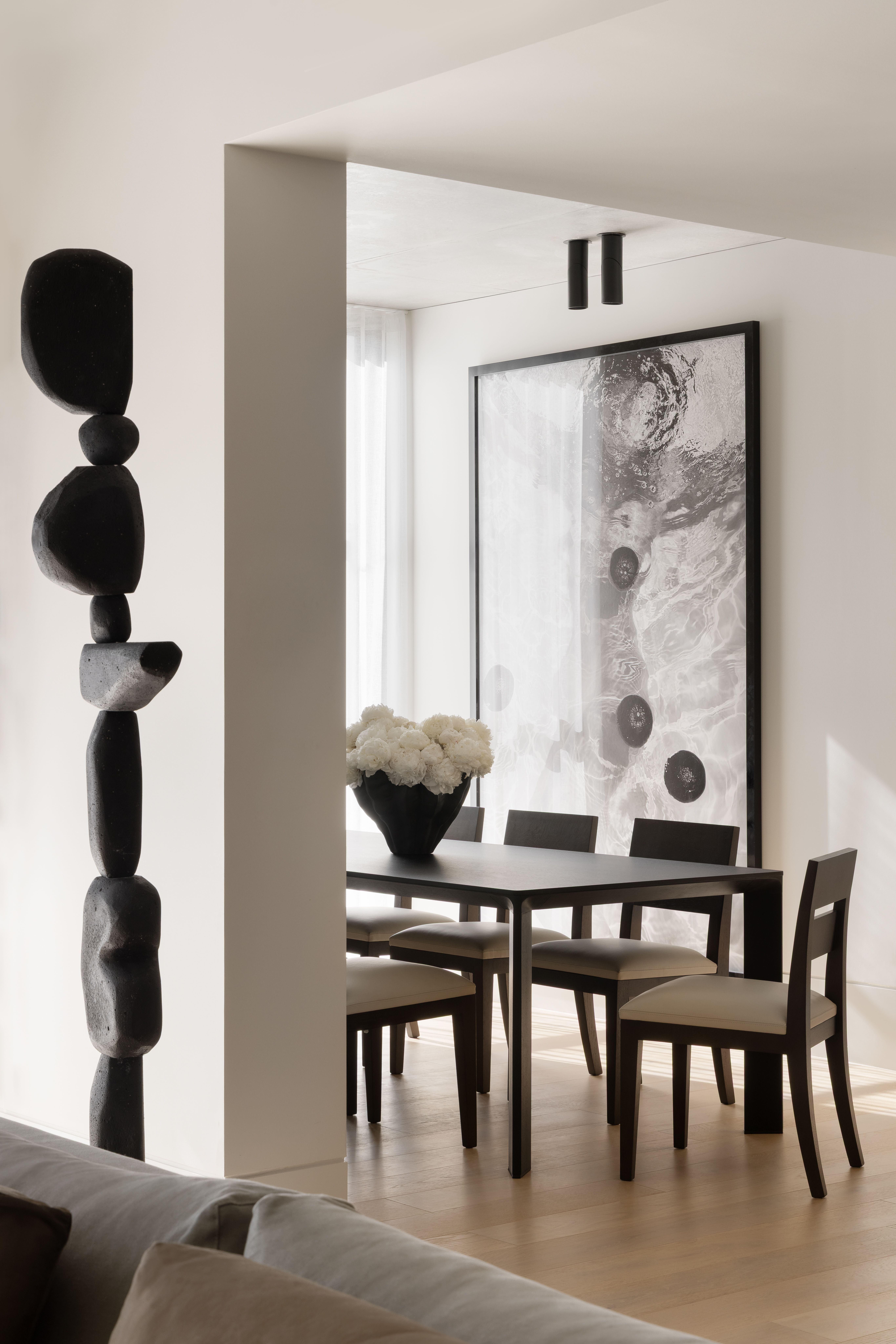 Sculptural black totem framing a dining room hung with abstract artwork