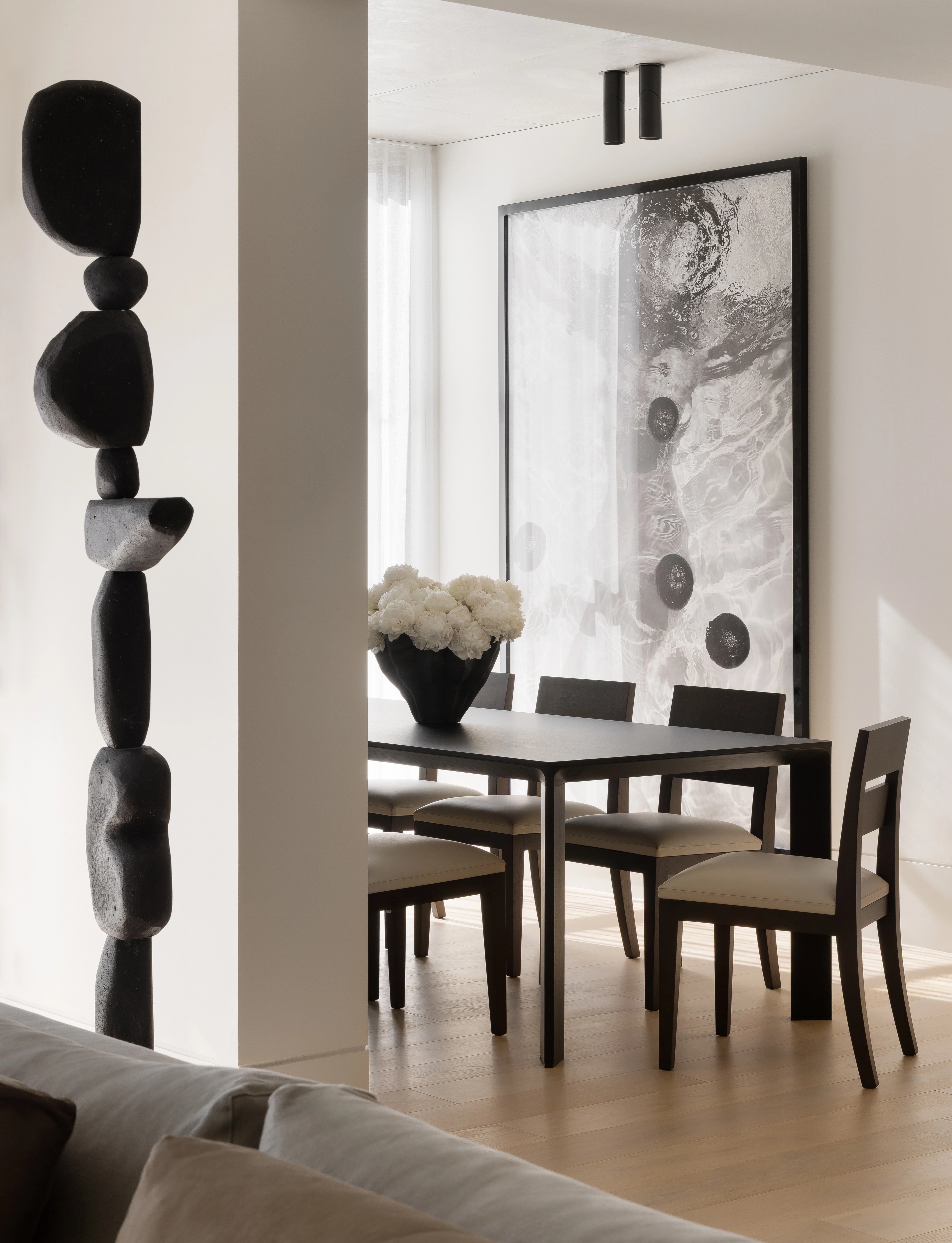 Sculptural black totem framing a dining room hung with abstract artwork