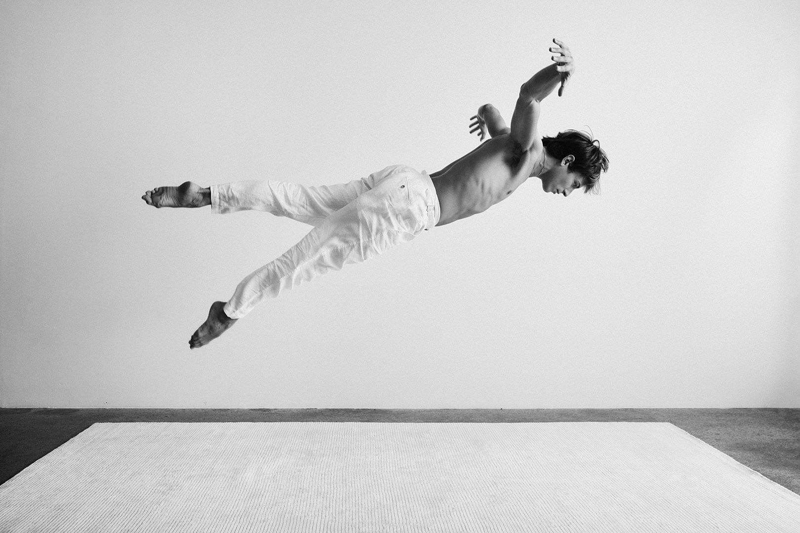 Man in white suspended mid-air above a bare floor in stark monochrome