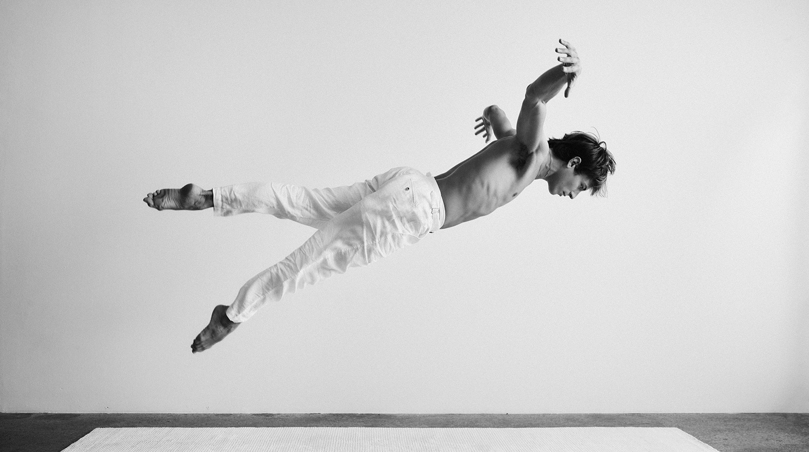 Man in white suspended mid-air above a bare floor in stark monochrome
