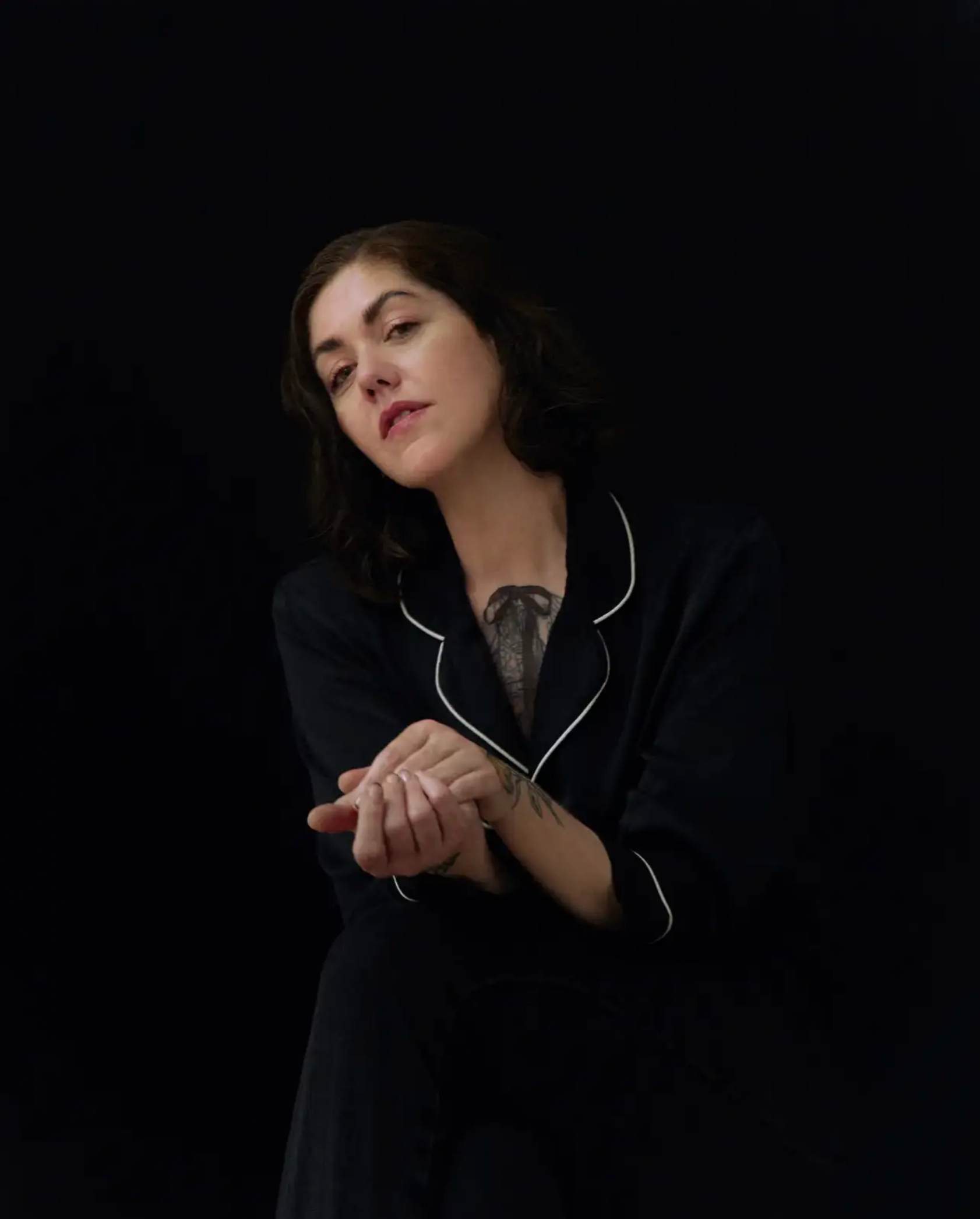 Woman in a dark silk robe cradling her hands against a black backdrop