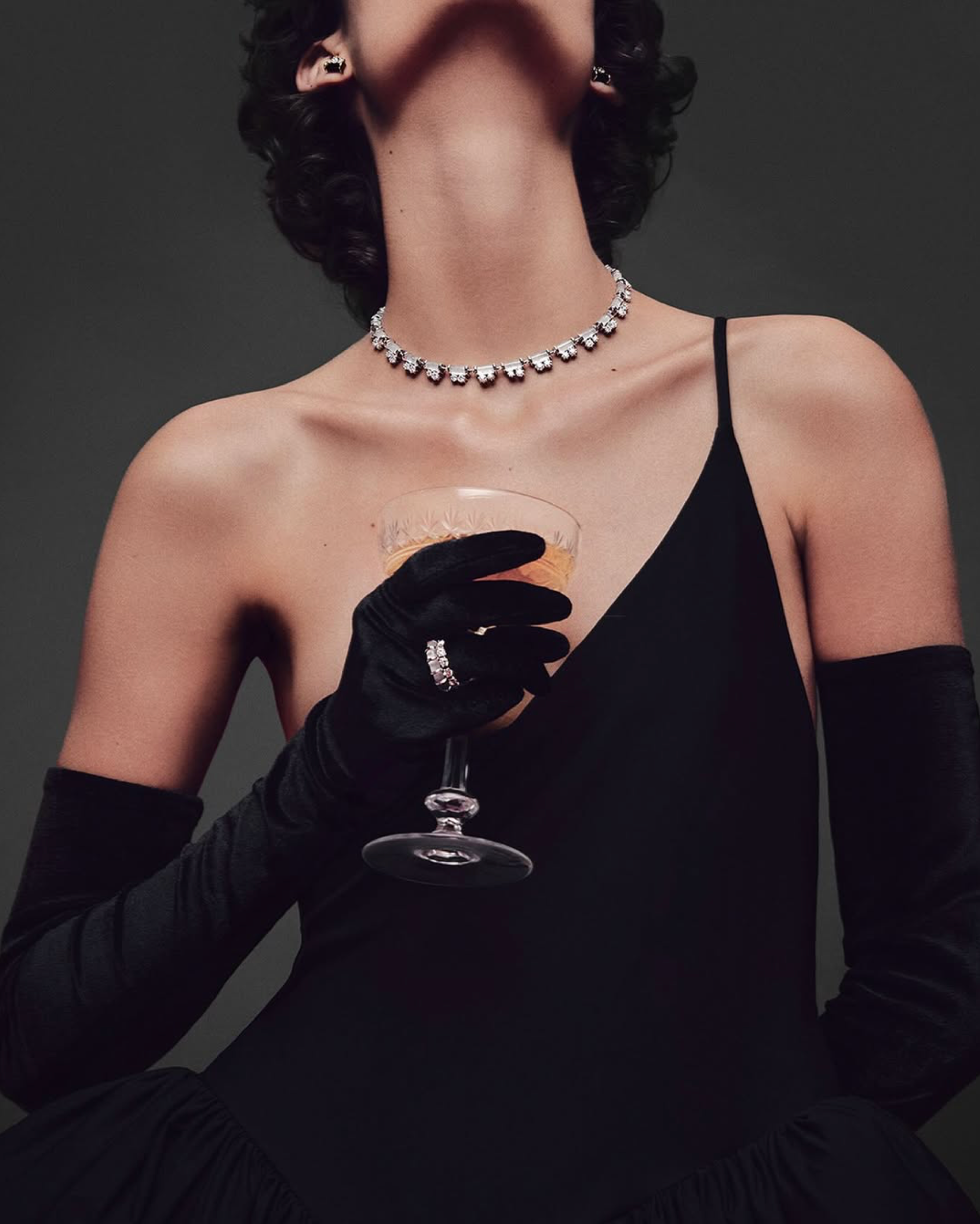 Model in black opera gloves and a diamond necklace raising a champagne coupe