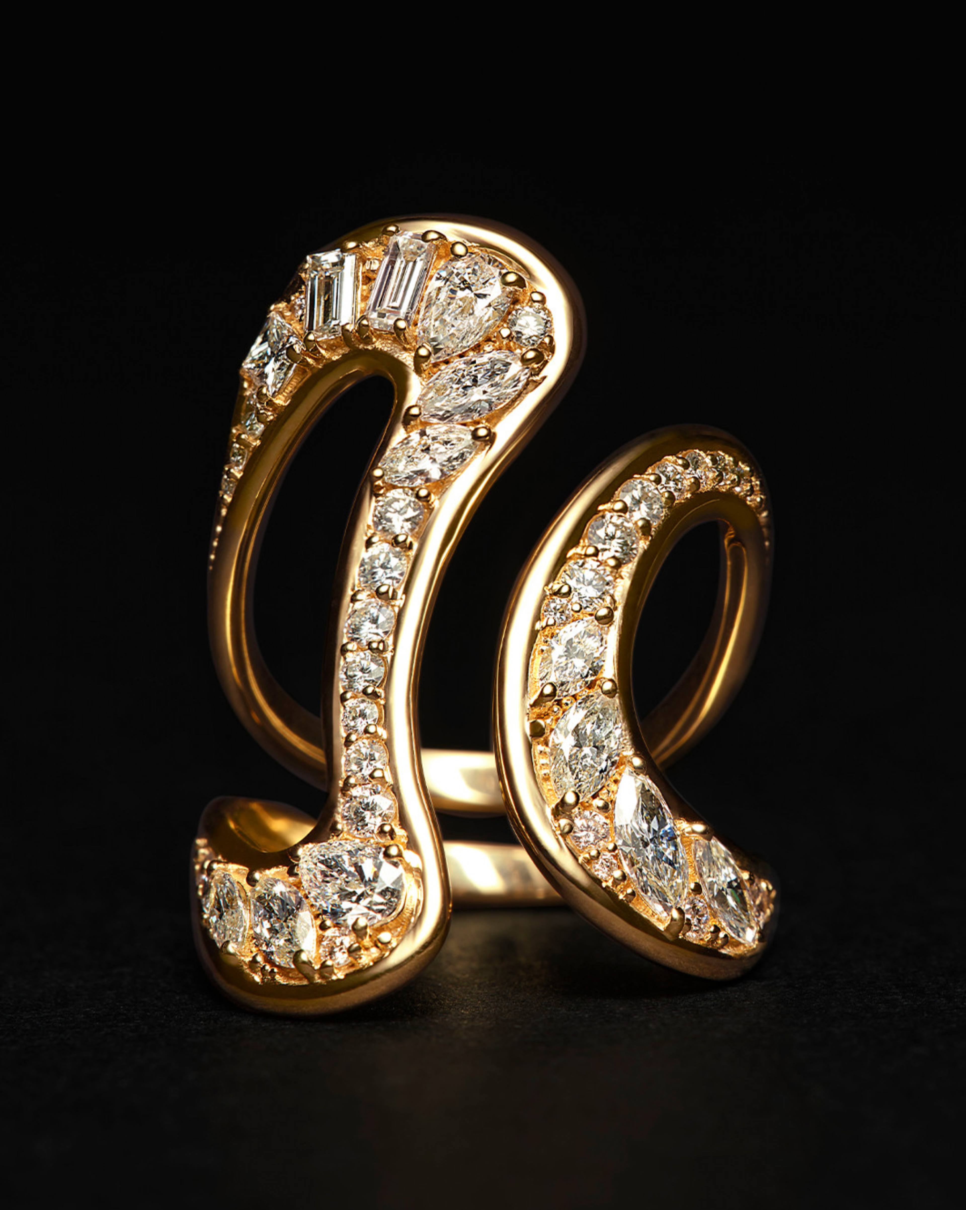 Swirling gold ring set with pavé diamonds, photographed on a dark surface