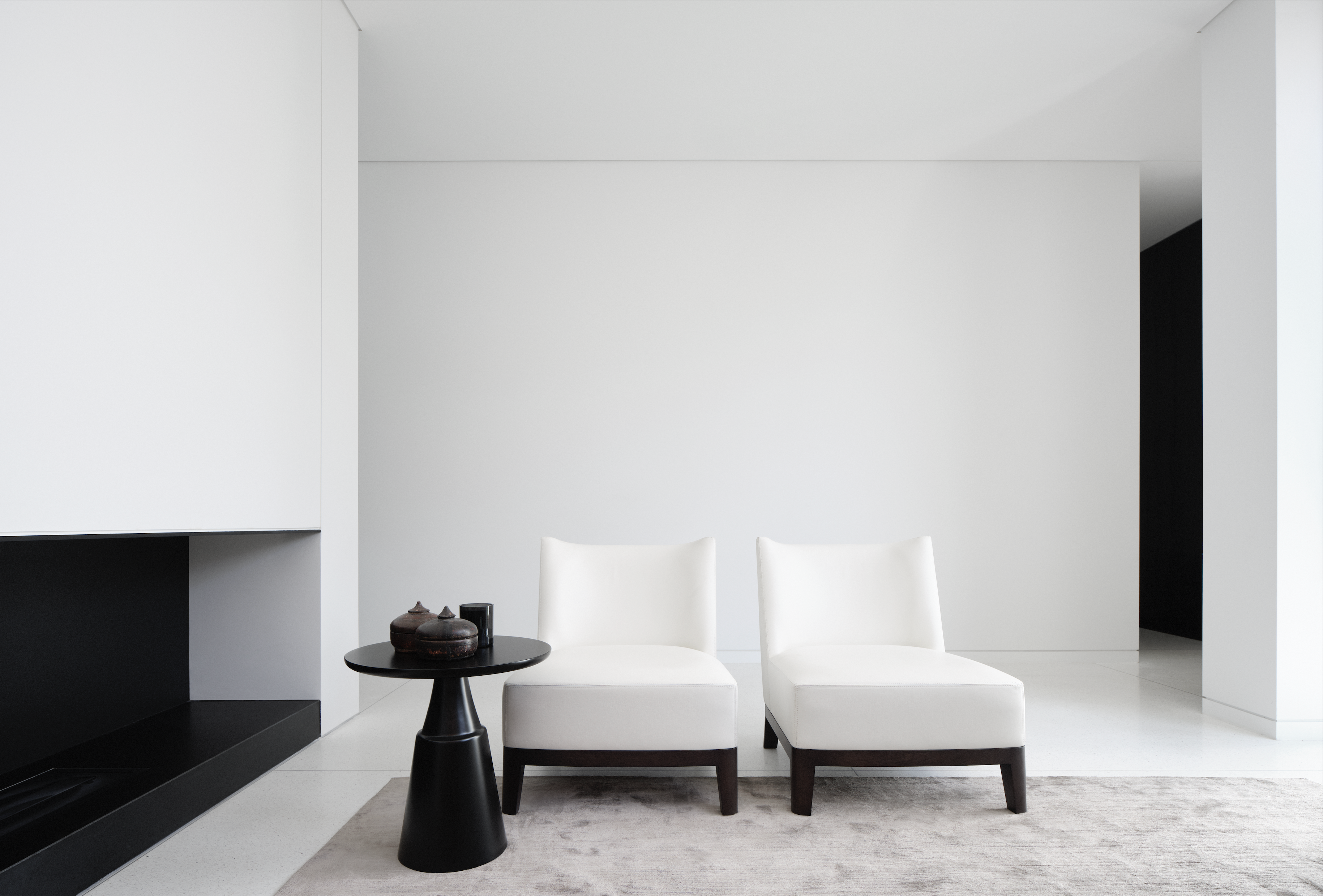 Minimalist white room with a black fireplace, two ivory slipper chairs and a round side table
