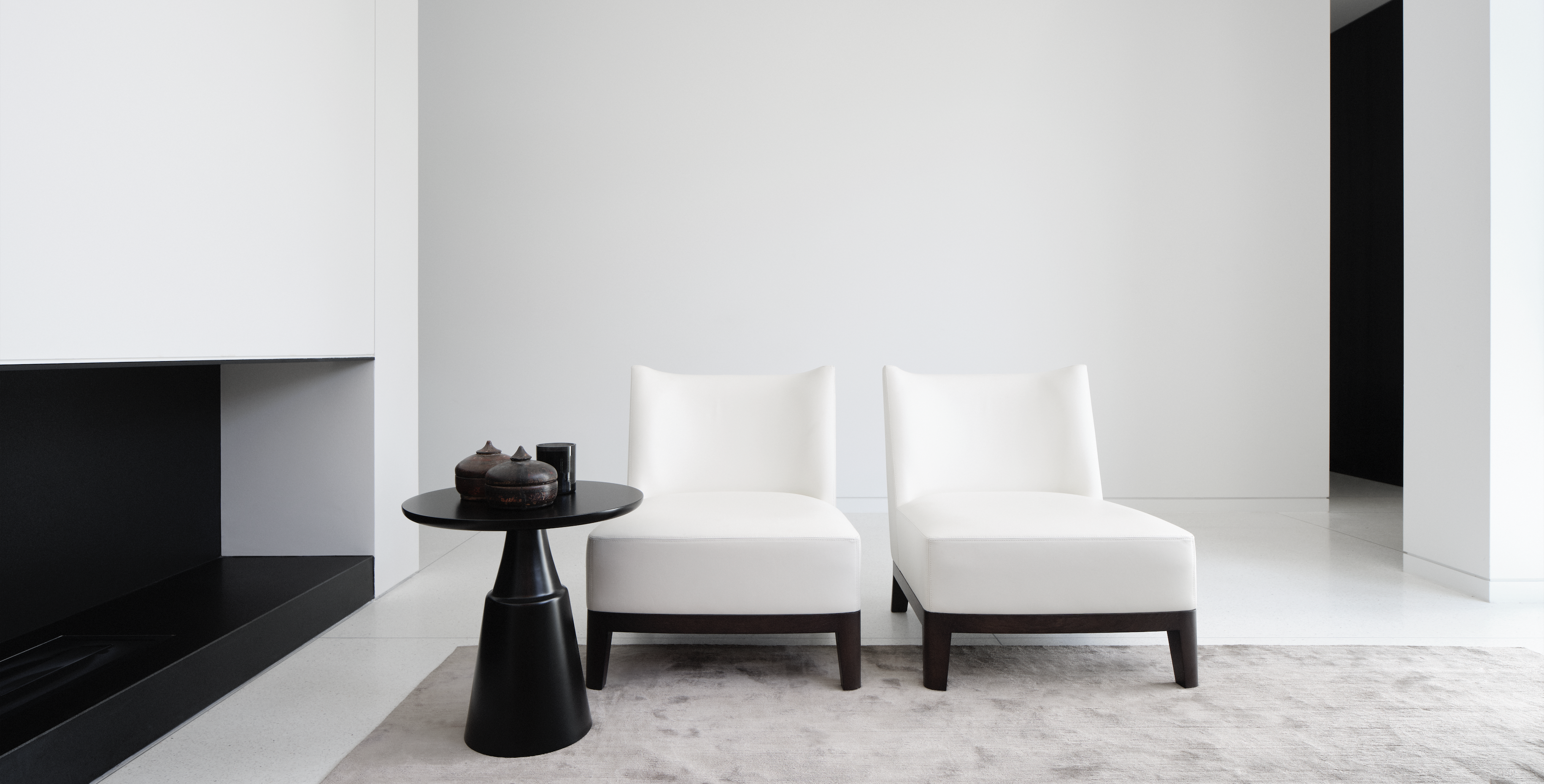 Minimalist white room with a black fireplace, two ivory slipper chairs and a round side table