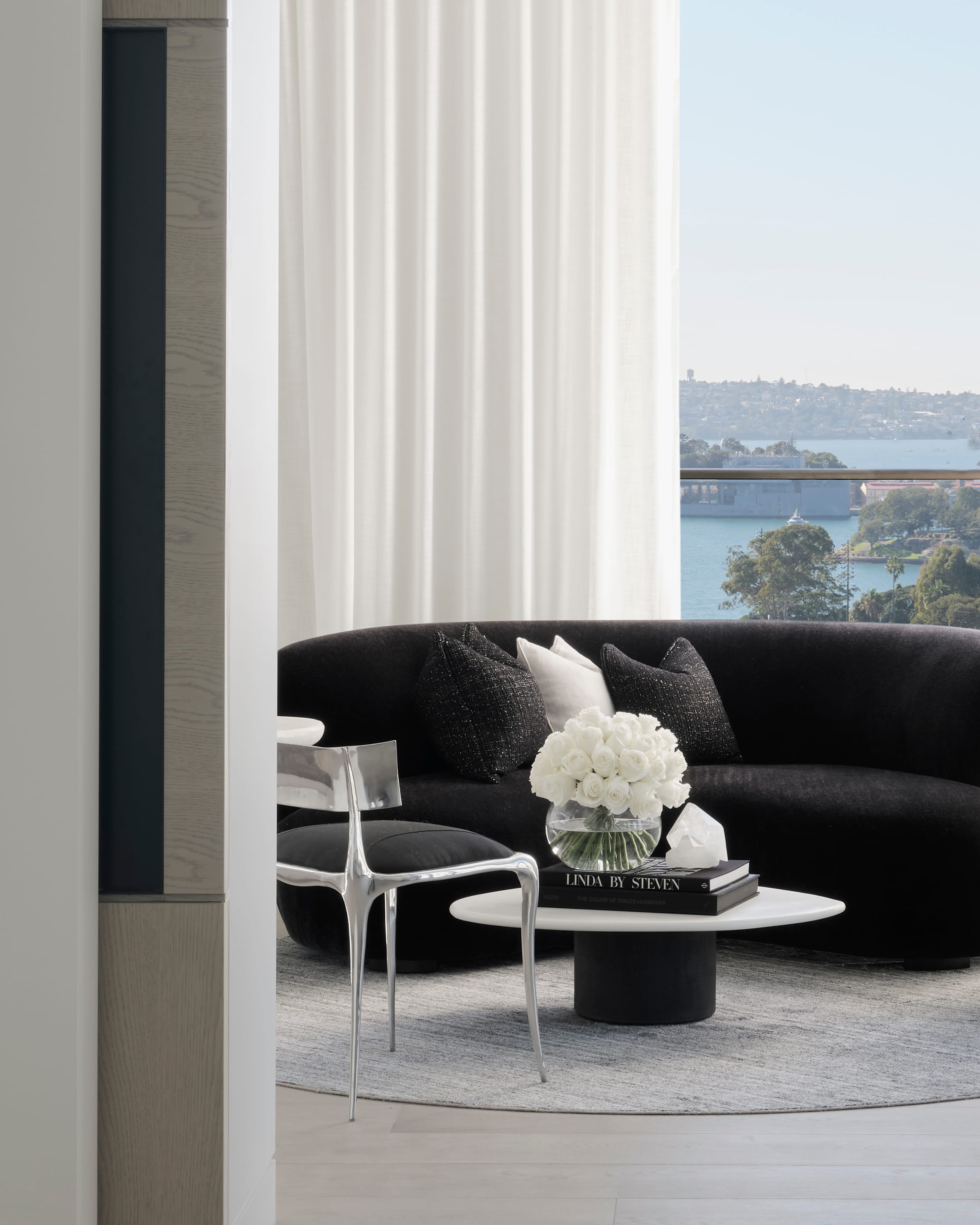 Curved black sofa and a sculptural white chair set against a sheer-veiled harbour view