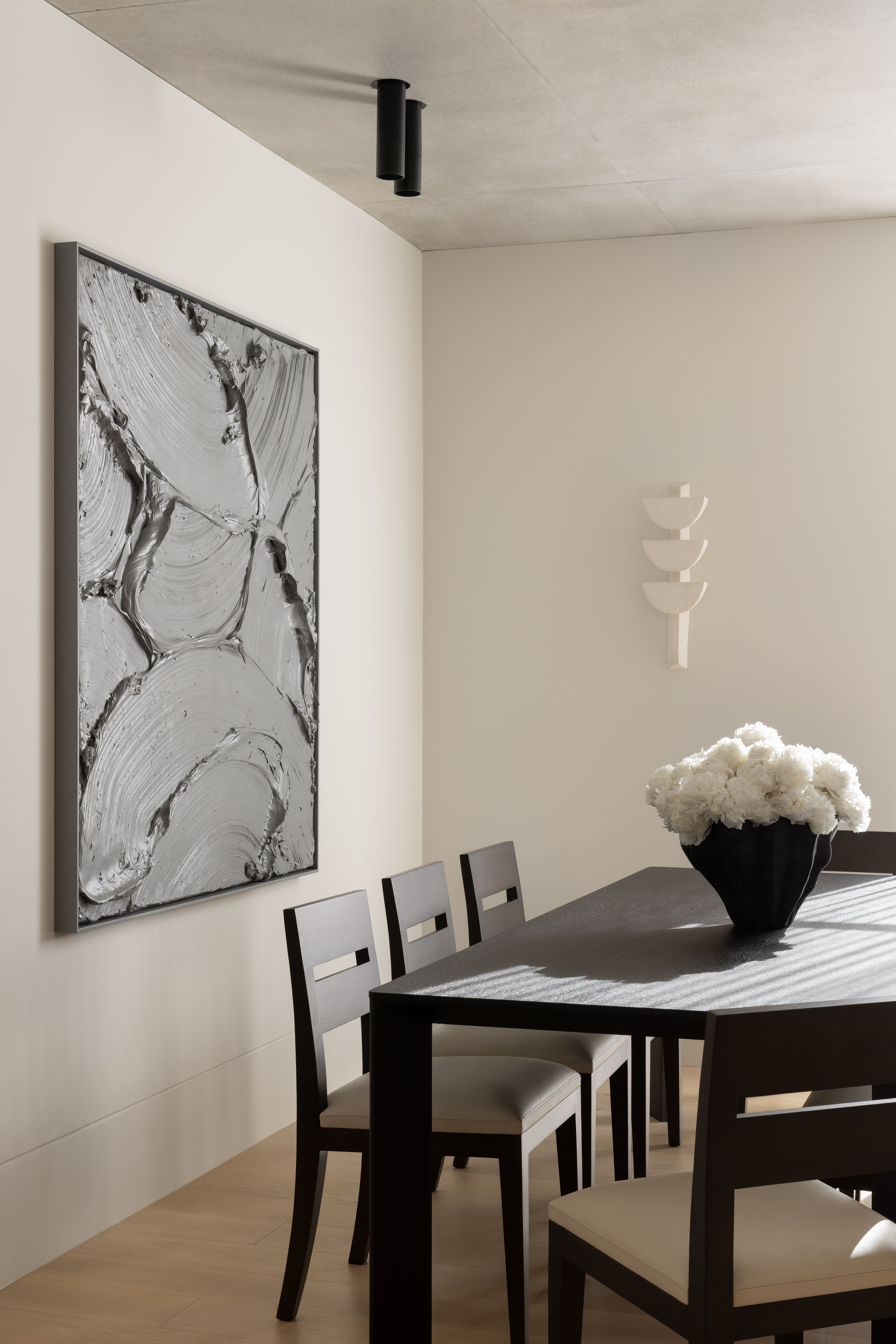 Dining vignette with a dark table, white peonies and a framed marbled artwork under a spotlight
