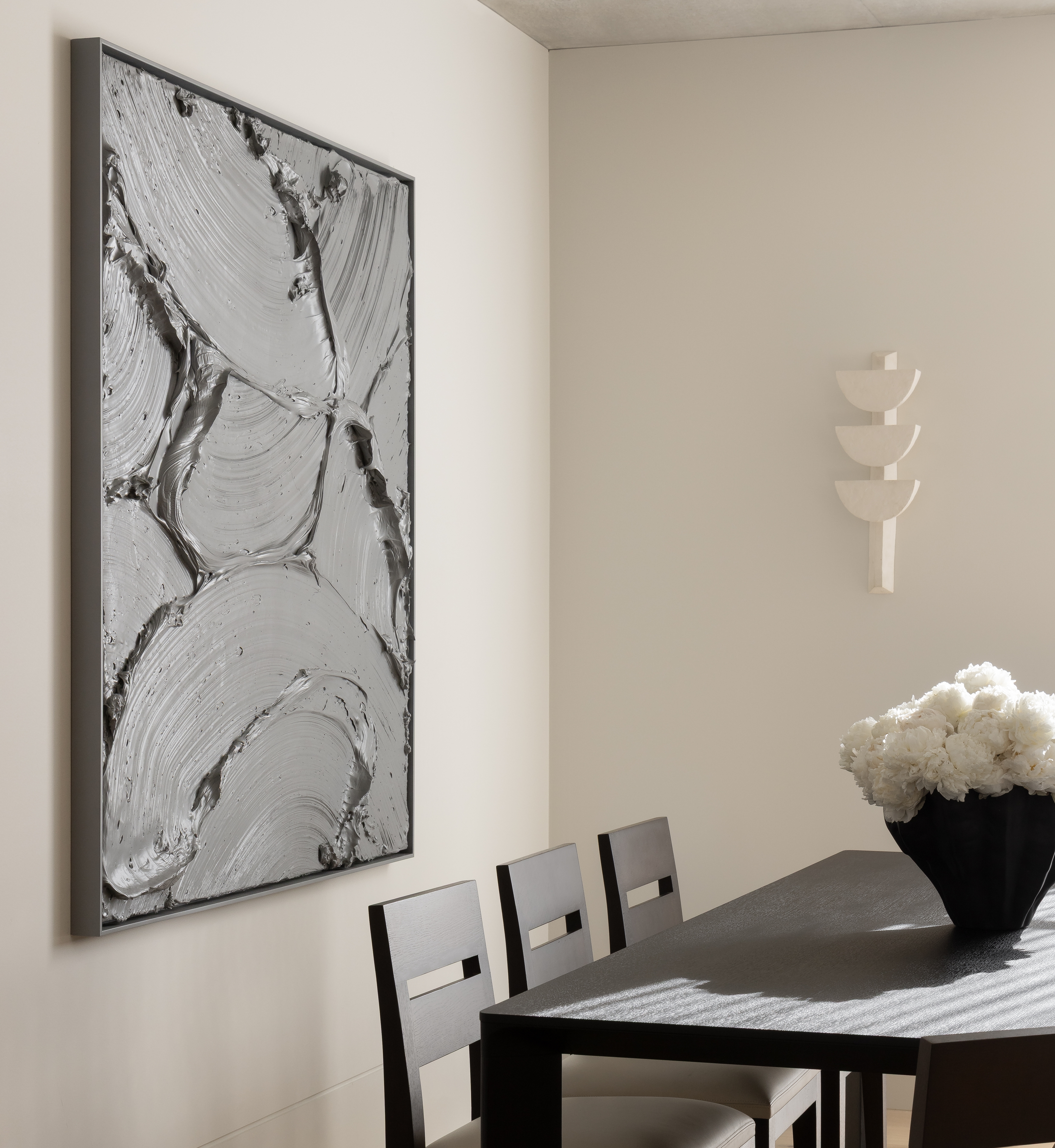 Dining vignette with a dark table, white peonies and a framed marbled artwork under a spotlight