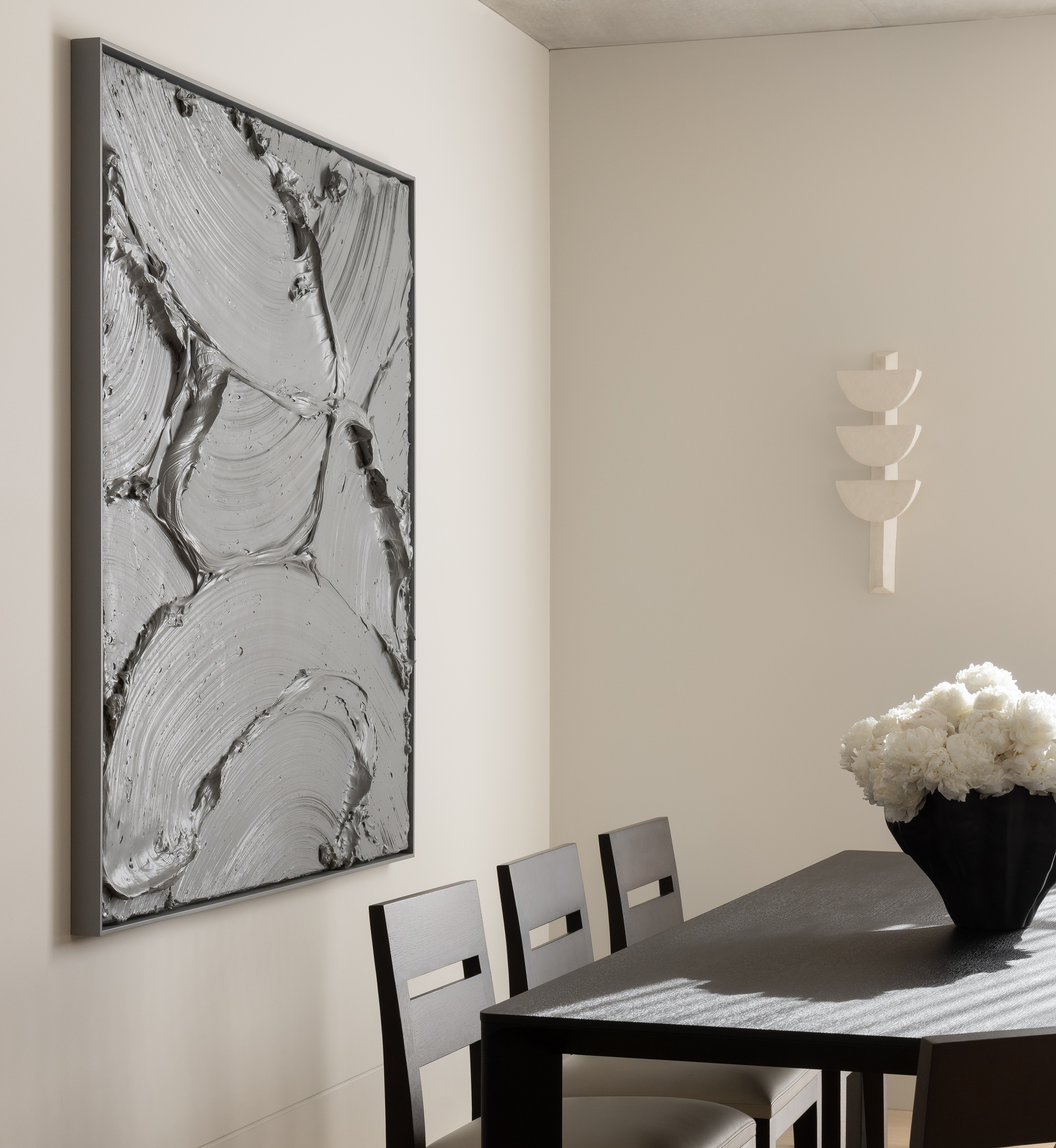 Dining vignette with a dark table, white peonies and a framed marbled artwork under a spotlight