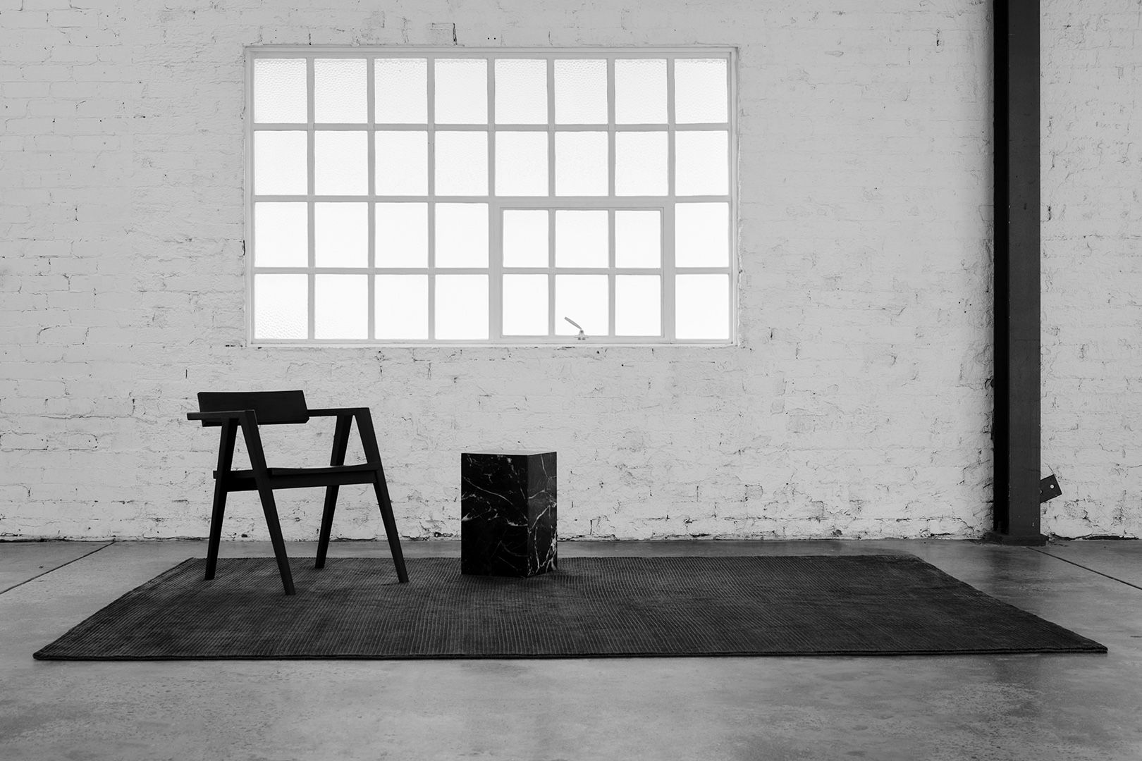 Spare loft with a black chair and cube beneath a gridded window