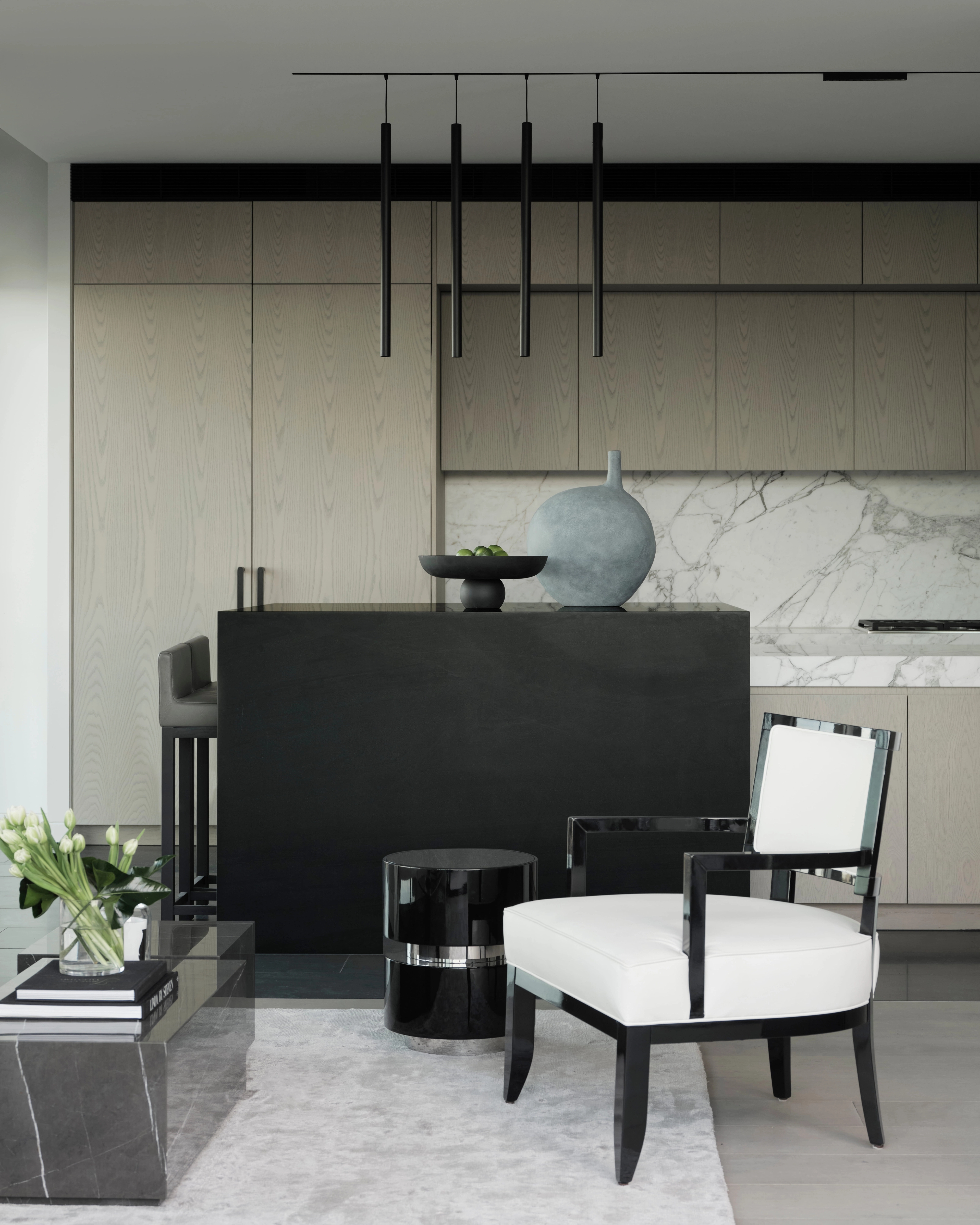 Black island and marble splashback meet a white armchair beneath a sculptural pendant cluster