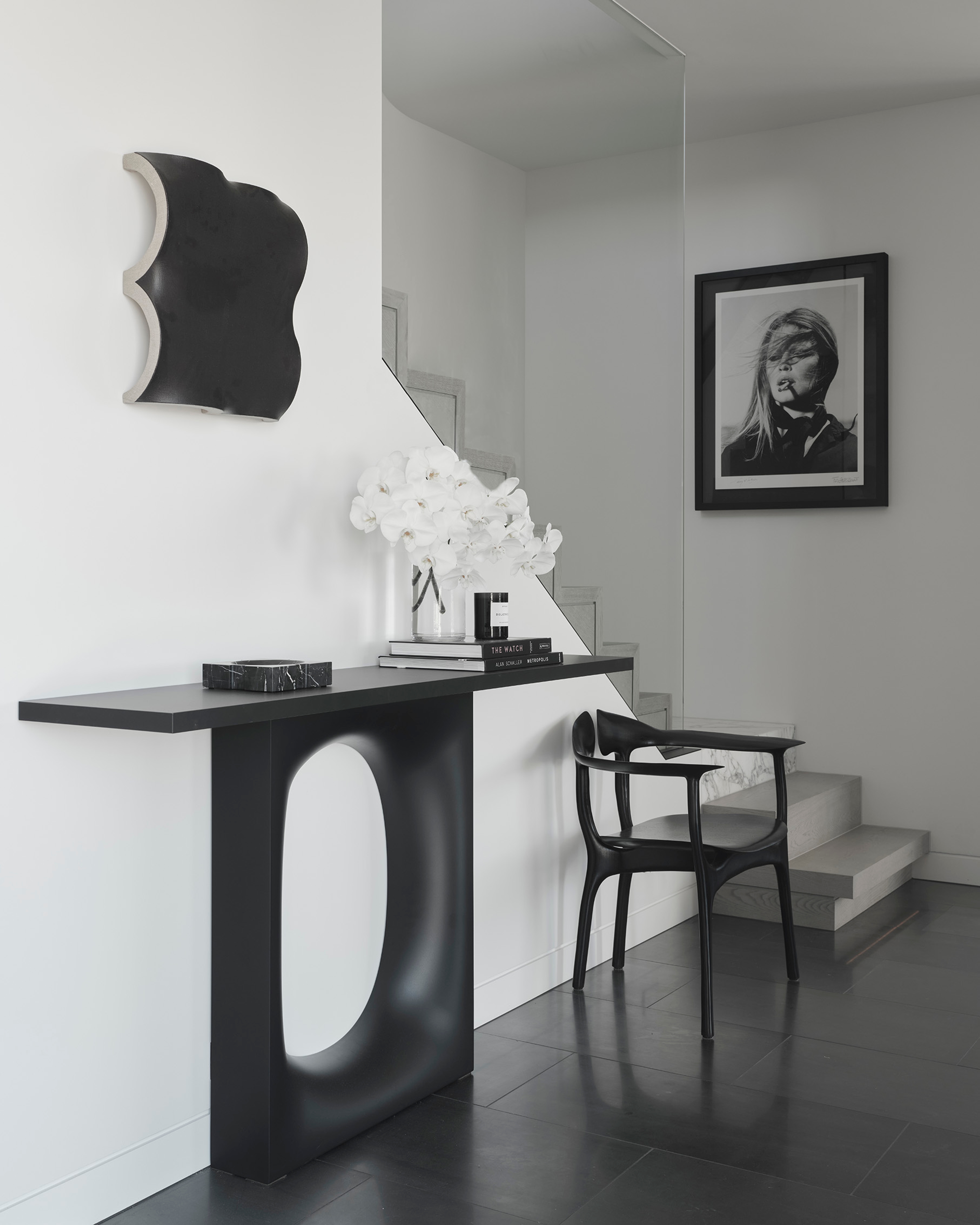 Entry vignette with a sculptural console, a framed portrait and a single white orchid
